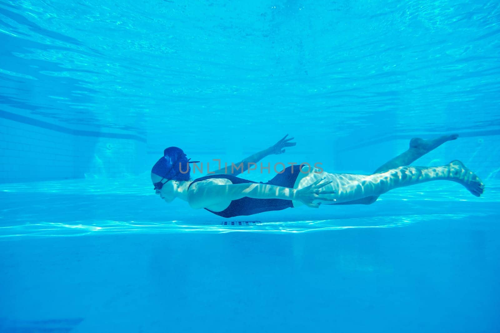 Young girl swimmer in swimsuit with goggles and swimming cap underwater in pool by VH-studio