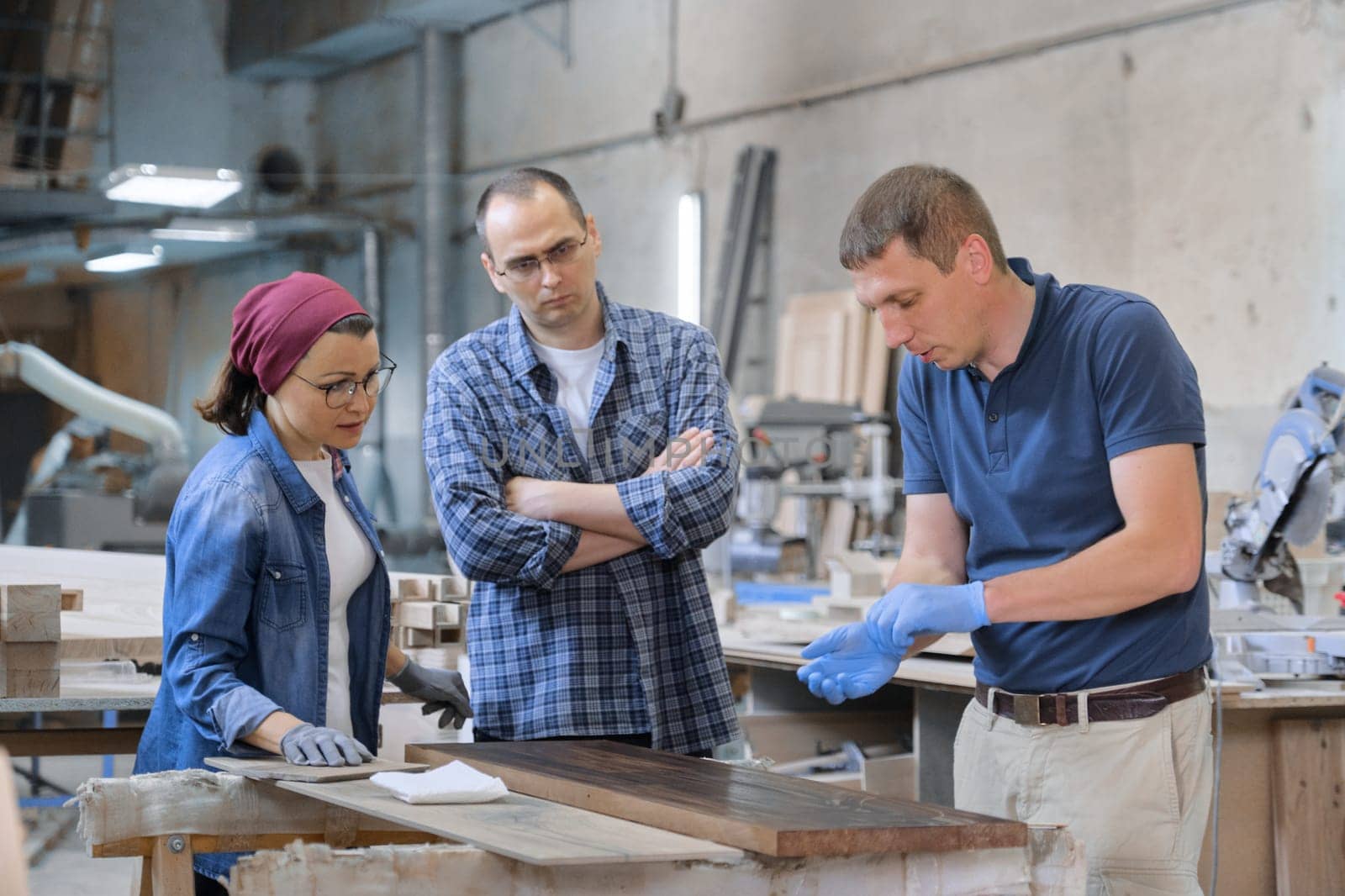 Group of people working in carpentry workshop, process of varnishing wooden board with oil. Furniture joinery wood business.