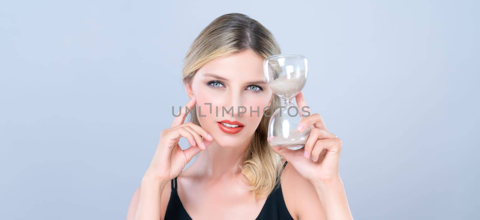 Alluring beauty model holding hourglass in forever young beauty concept of anti-aging skincare treatment for woman. Beautiful caucasian women portrait with perfect makeup in isolated background.