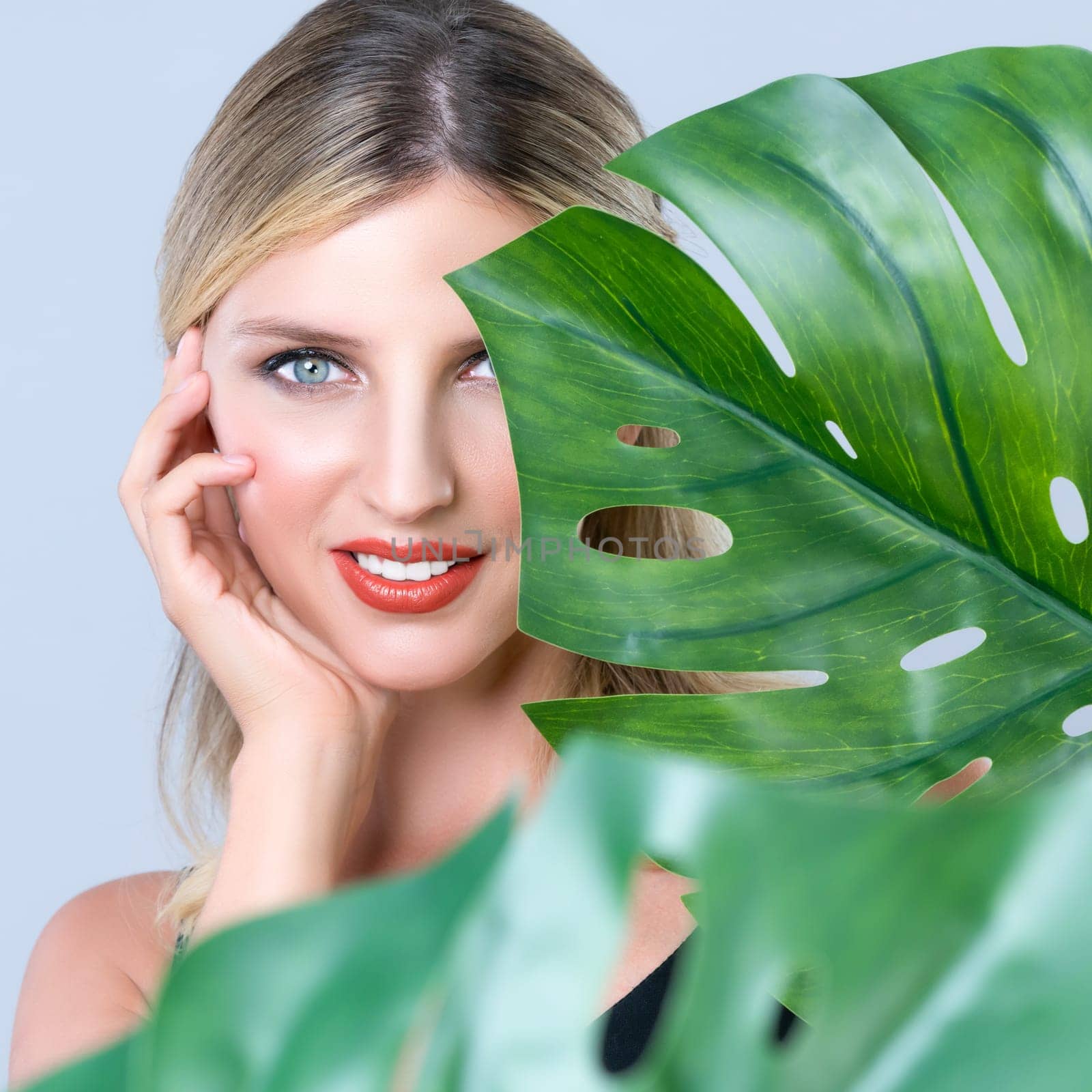 Closeup woman with perfect clean skin and alluring flawless natural soft facial makeup holding green leave monstera. Natural skincare treatment beauty or spa concept in isolated background.