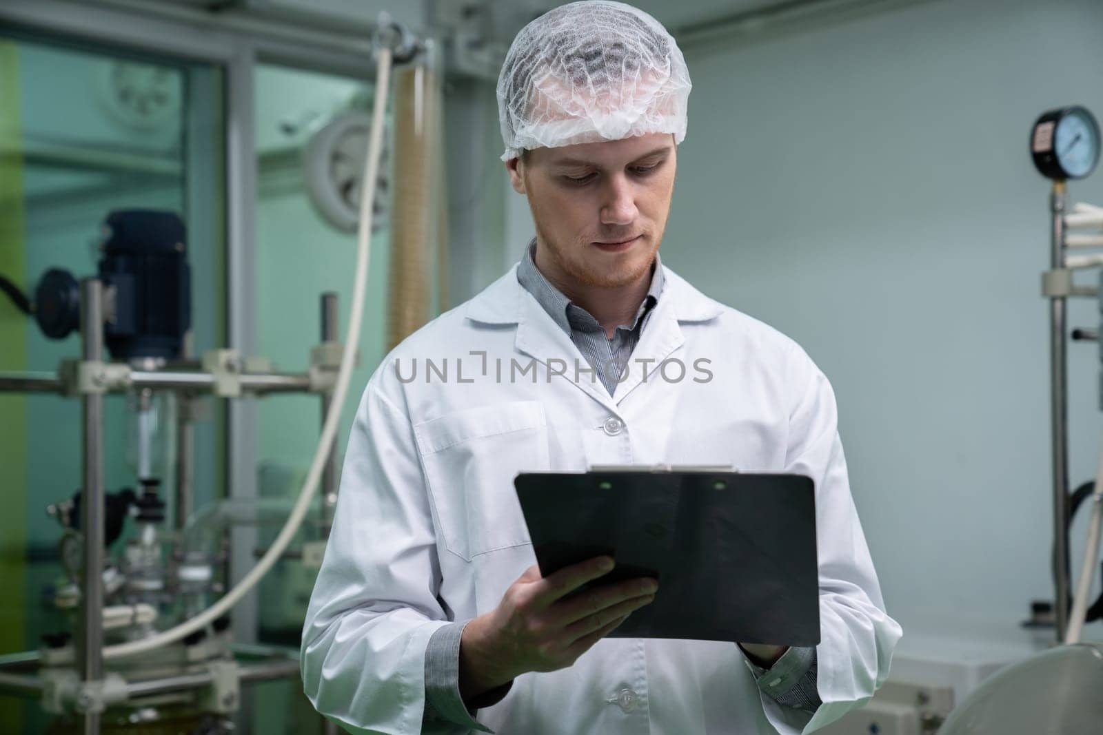 Apothecary scientist using a clipboard and pen to record information from a CBD oil extractor and a scientific machine used to create medicinal cannabis products.