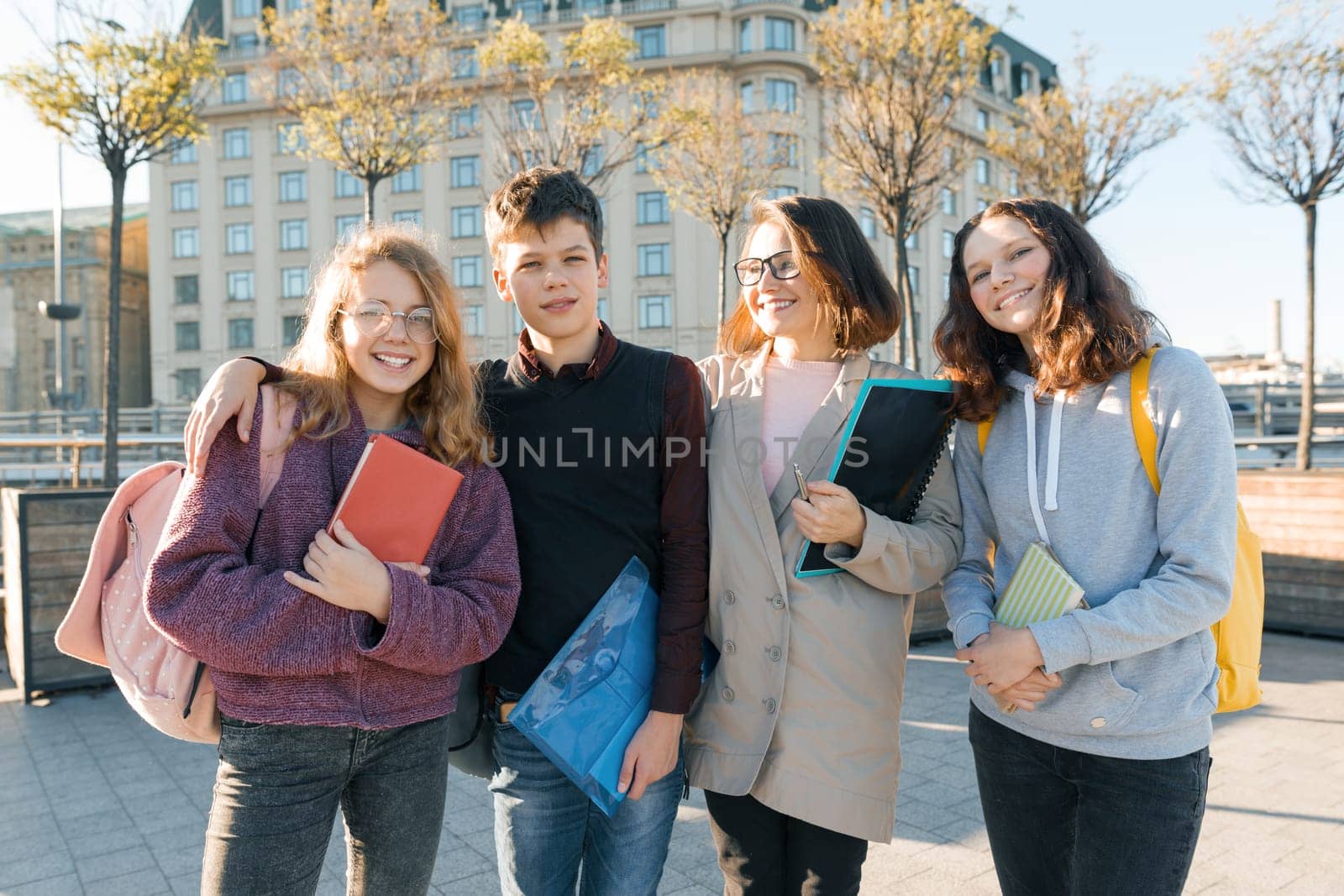 Outdoor portrait of a female teacher and group of teenage students, golden hour.