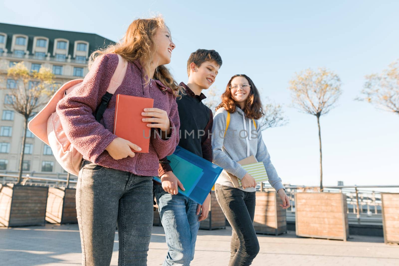 Outdoor portrait of teenage students with backpacks walking and talking. City background, golden hour.