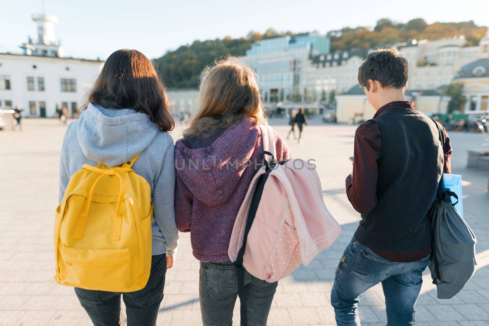 View from the back on three high school students. City background, golden hour.