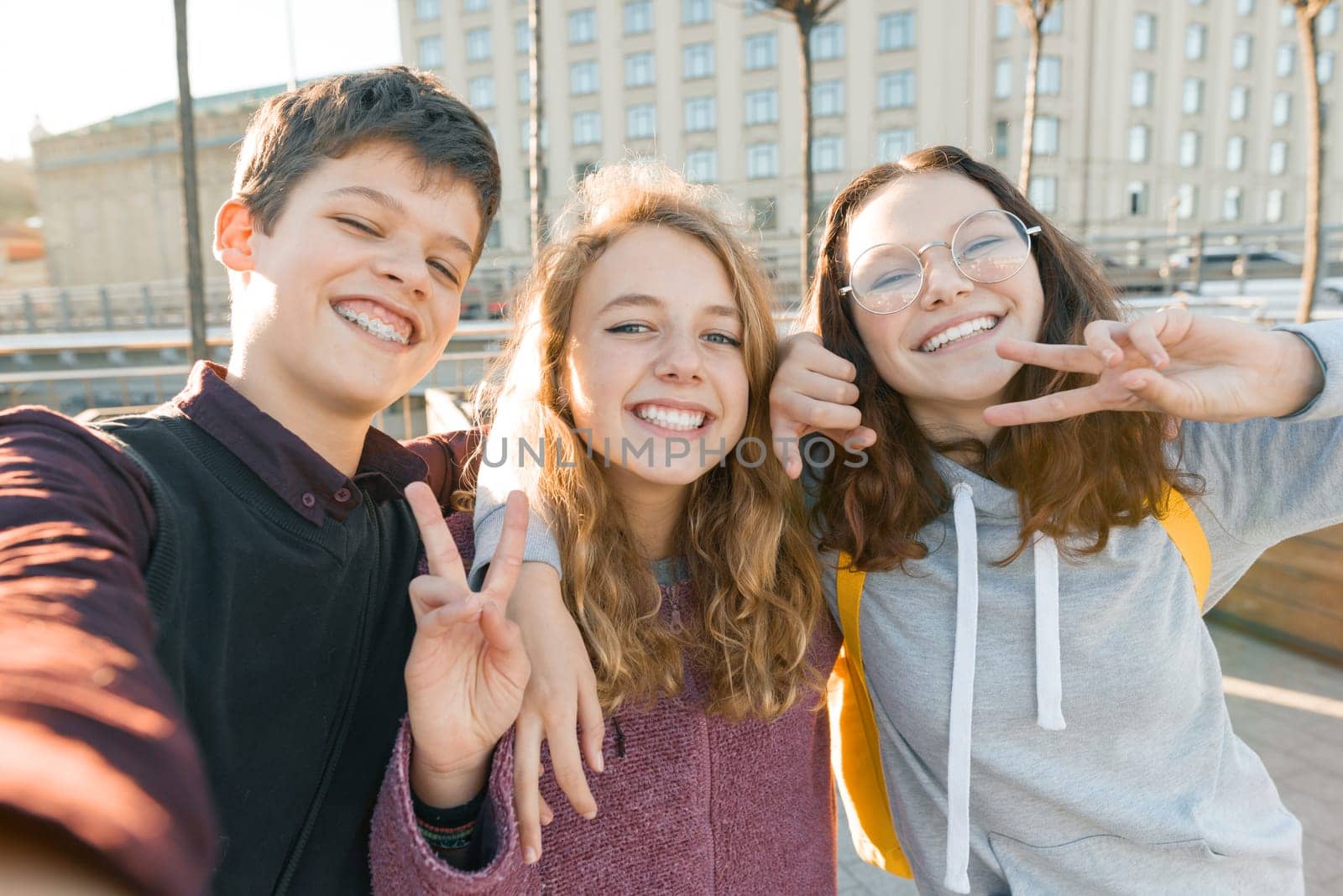 Portrait of three teen friends boy and two girls smiling and taking a selfie outdoors by VH-studio