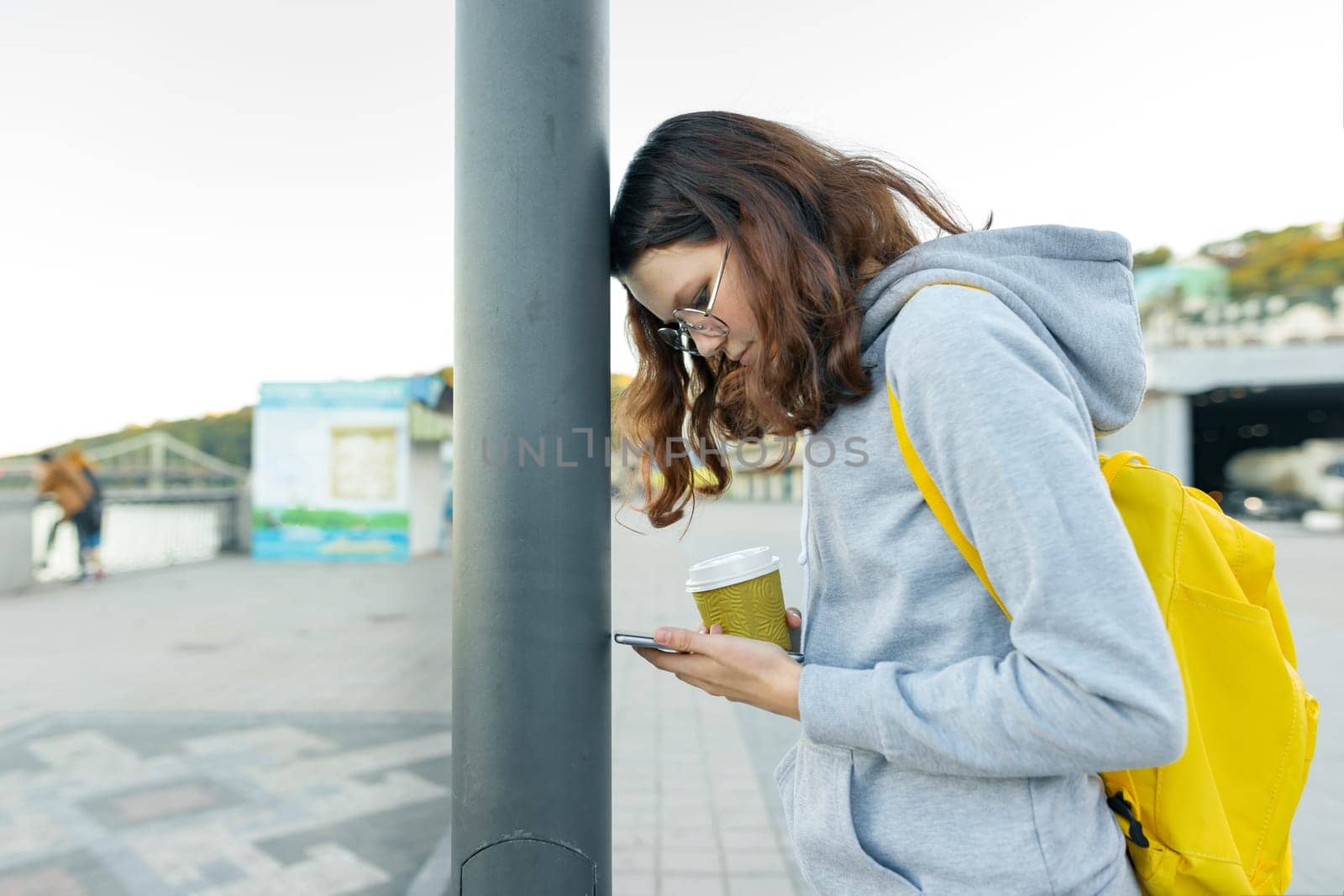 Smart focused girl is distracted by mobile phone, girl reading smartphone, head on a pole