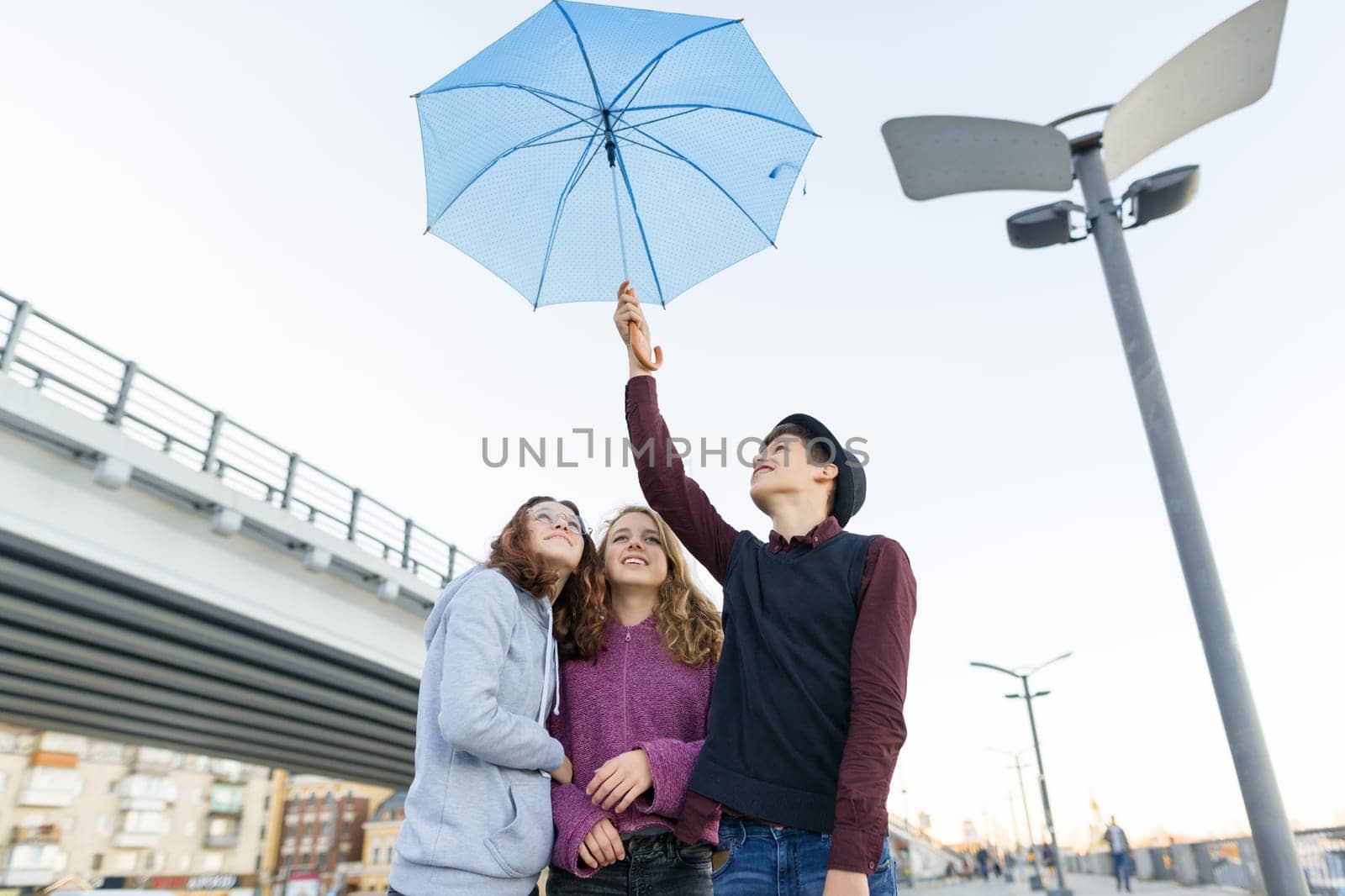 Group of teenagers friends having fun in the city, laughing kids with umbrella. Urban teen lifestyle