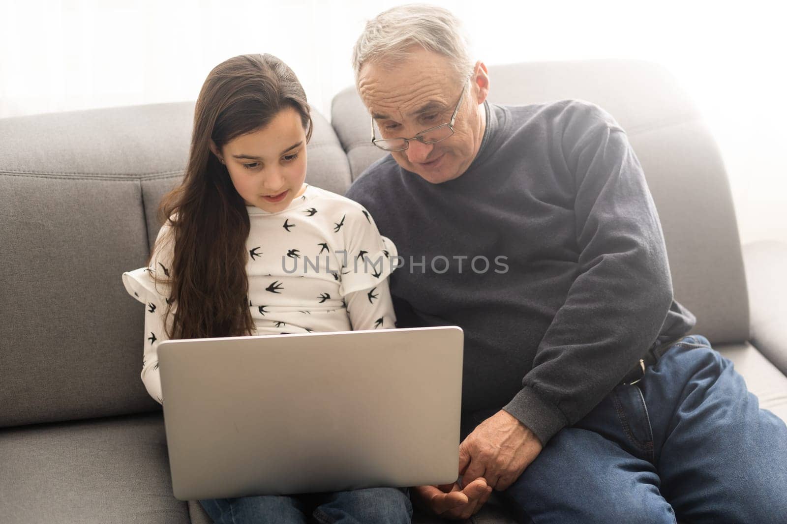 Happy retirement grandfather and pretty granddaughter laughing while watching e-book for learning to education together by laptop. Family educational at home concept. Technology and education. by Andelov13