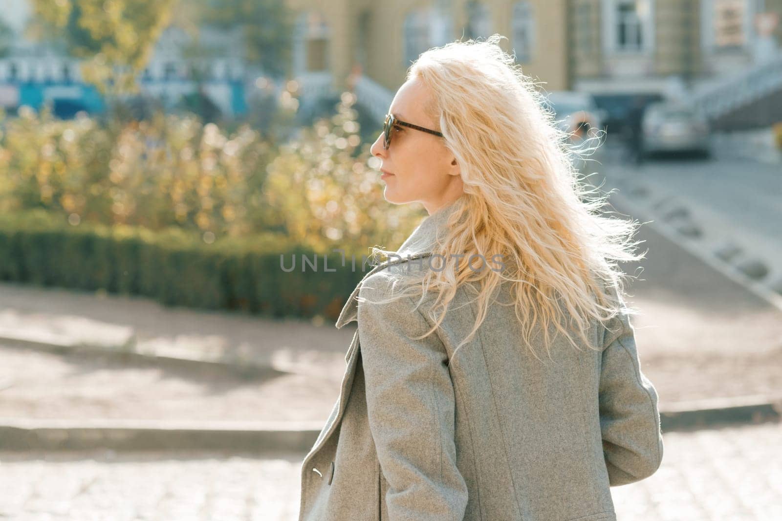 Closeup outdoor portrait of young smiling blond woman with sunglasses with long curly hair. On city street sunny day.