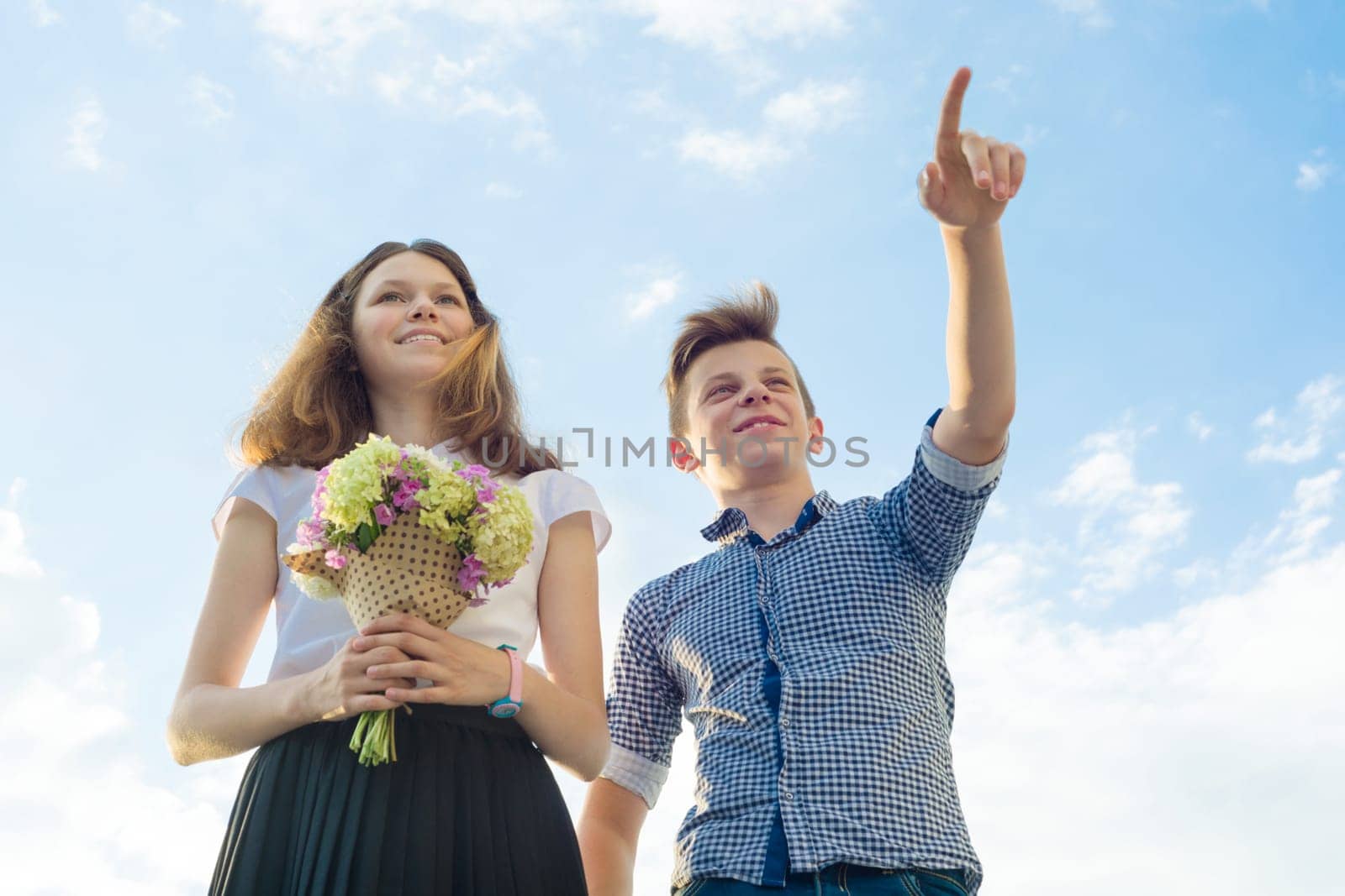 Happy couple of teens boy and girl 14, 15 years old. Young people smiling and talking, blue sky background.