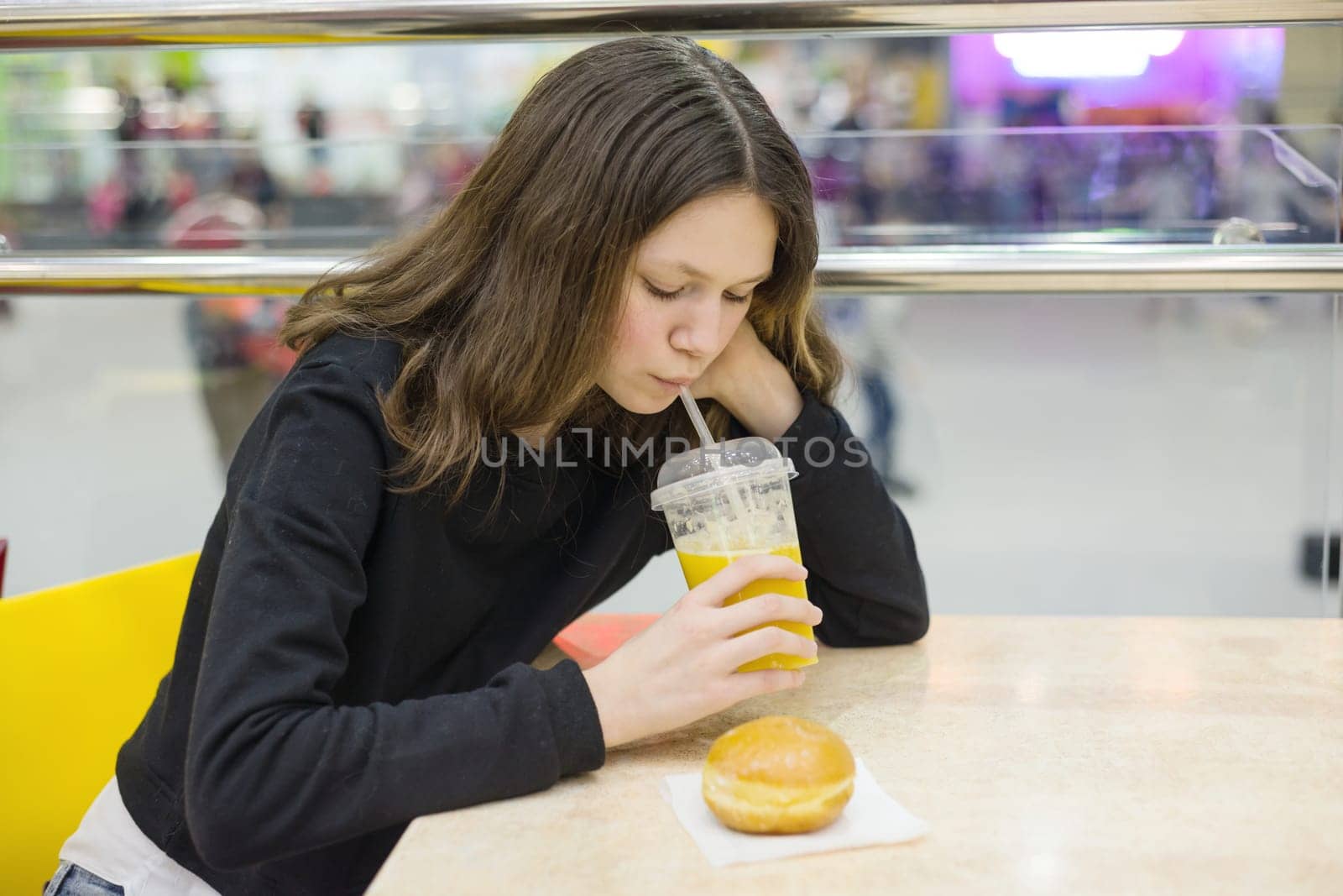 Teenage girl sitting at a table eating cake and drinking juice, break on food.