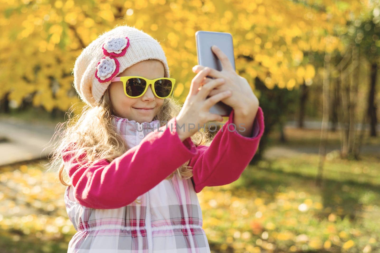 Pretty girl of 7 years doing selfie using smartphone, autumn background