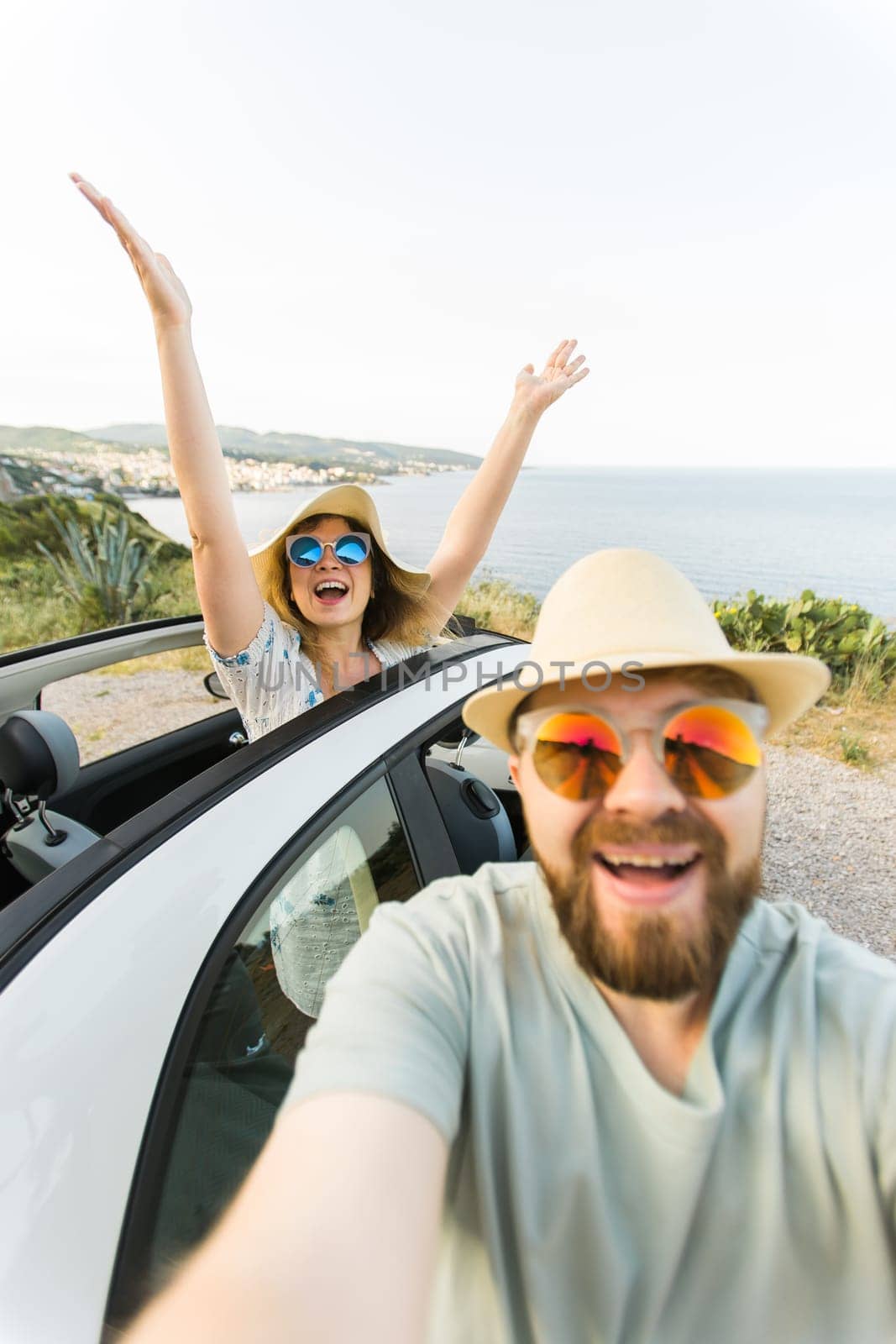 Happy beautiful couple in love taking a selfie portrait driving a convertible car on the road at vacation. Rental cars and vacation by Satura86