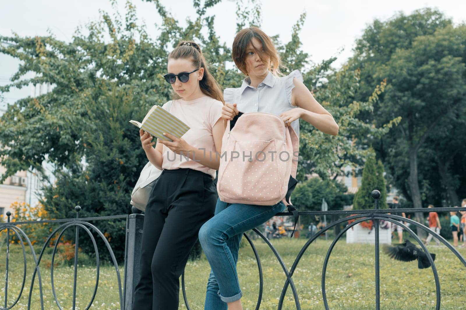 Two learning girls students with backpacks and textbooks outdoor in a park.
