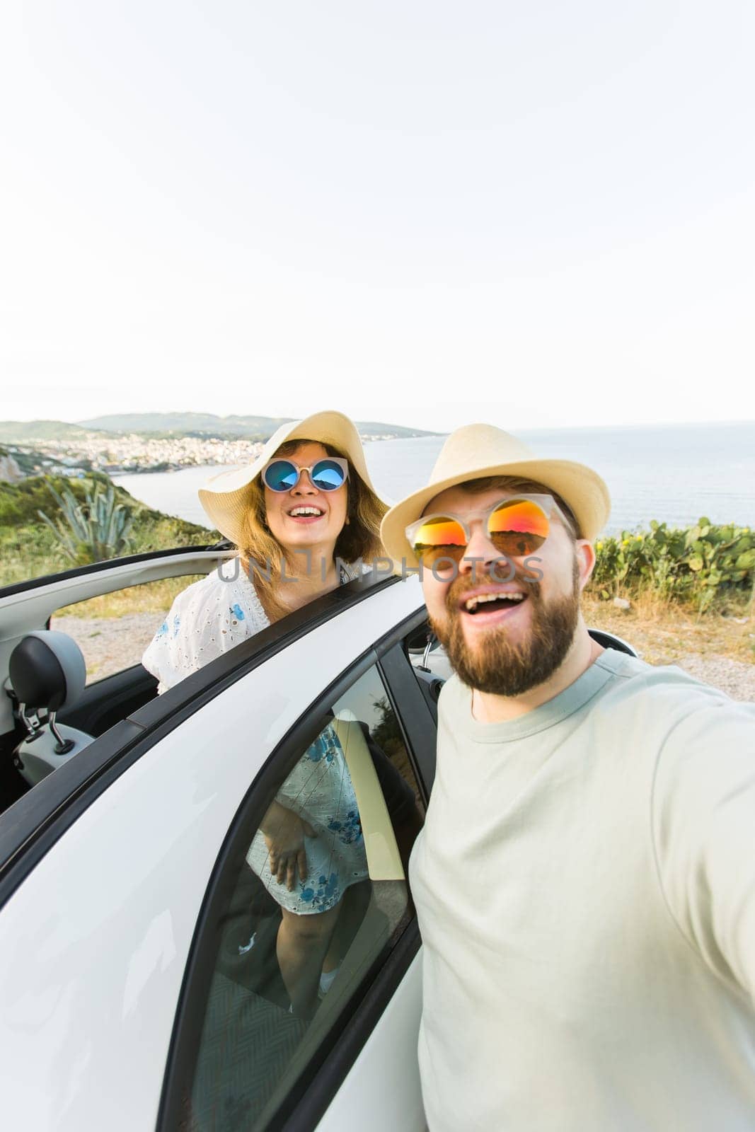 Romantic couple making selfie on smartphone camera in rental cabrio car on ocean or sea beach, enjoying summer vacation together and taking picture cellular resting near sea on weekends