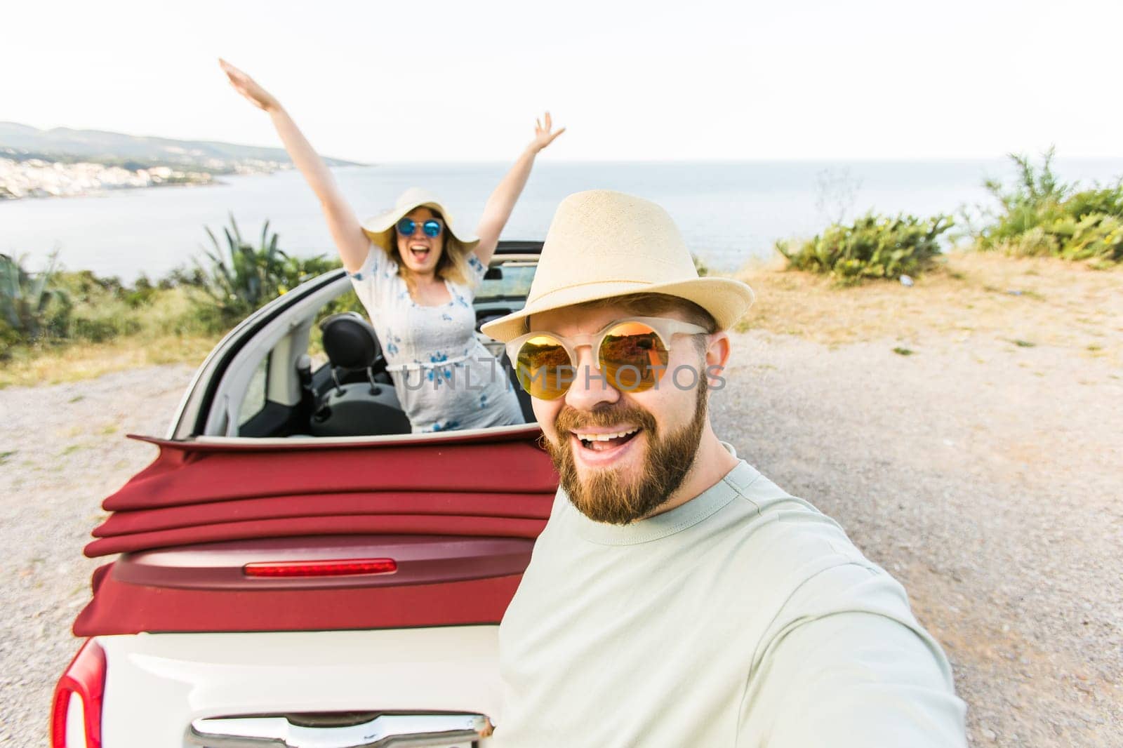 Happy beautiful couple in love taking a selfie portrait driving a convertible car on the road at vacation. Rental cars and vacation concept