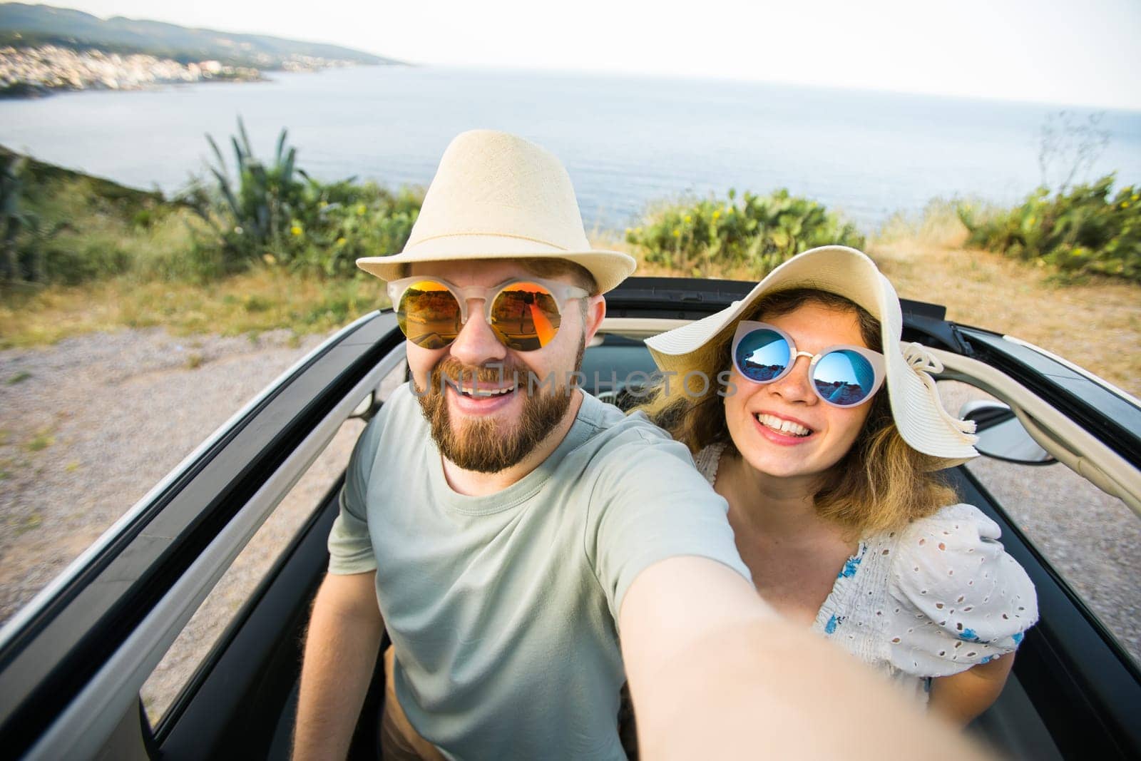 Romantic couple making selfie on smartphone camera in rental cabrio car on ocean or sea beach enjoying summer vacation together and taking picture on cellular resting near sea on weekends by Satura86