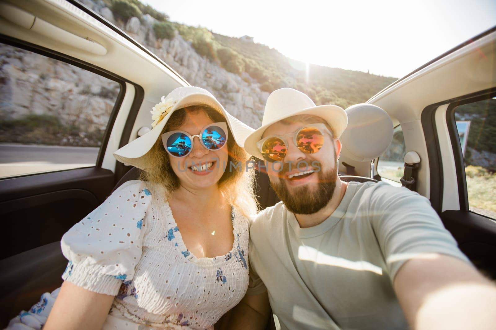 Happy beautiful couple in love taking a selfie portrait driving a convertible car on the road at vacation. Rental cars and vacation concept