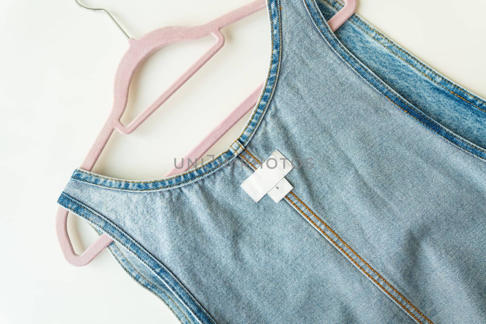 Denim clothes on a hanger. White label on denim clothes with size and brand, place for writing, mockup. Close-up. by sfinks