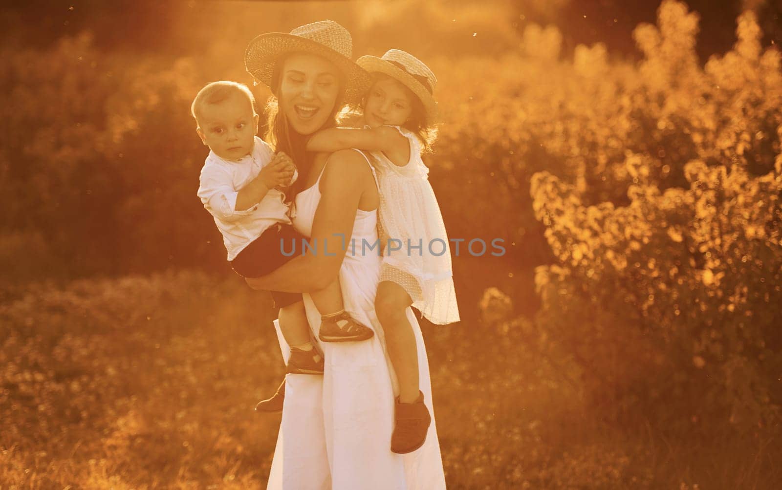 Happy family of mother, little son and daughter spending free time on the field at sunny day time of summer by Standret