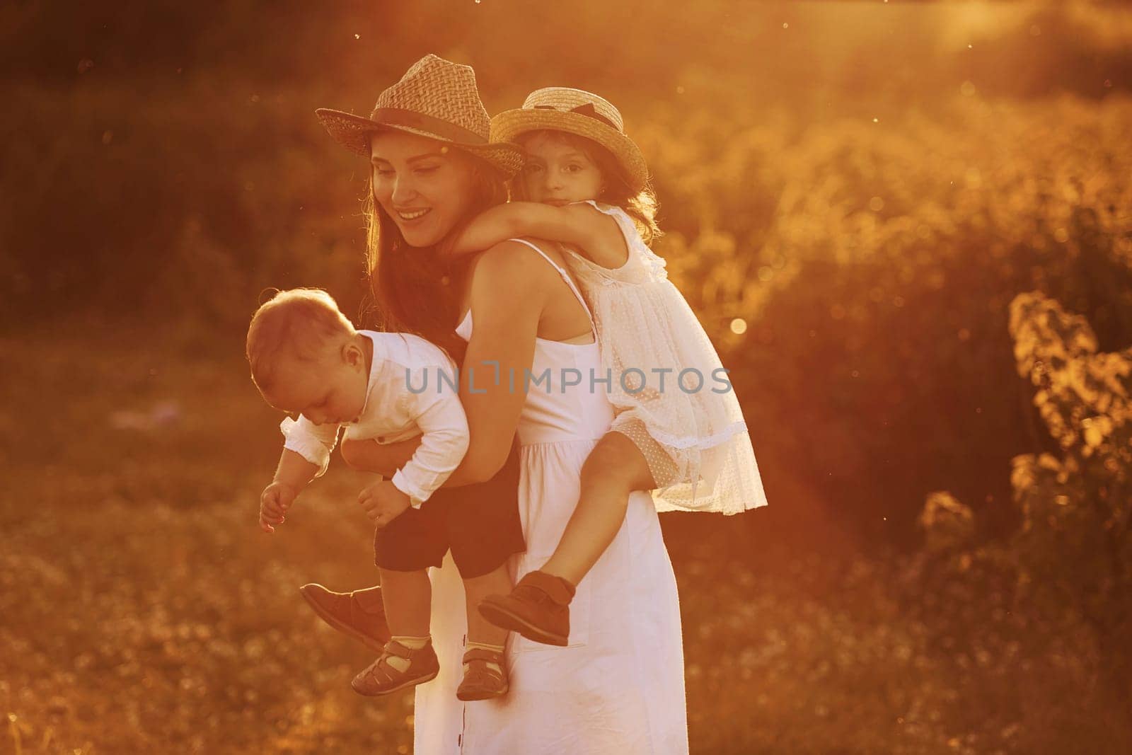 Happy family of mother, little son and daughter spending free time on the field at sunny day time of summer by Standret