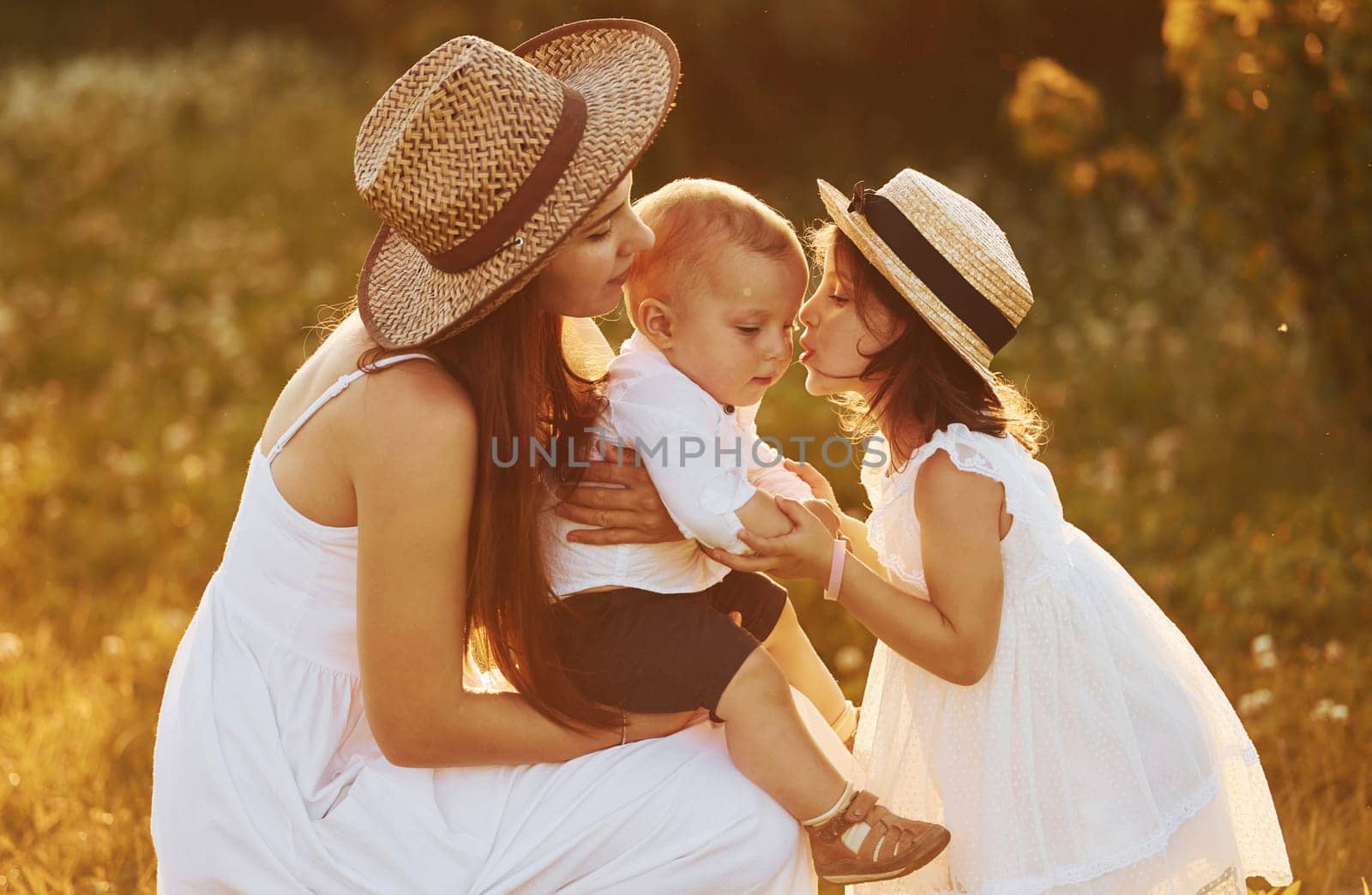 Happy family of mother, little son and daughter spending free time on the field at sunny day time of summer.