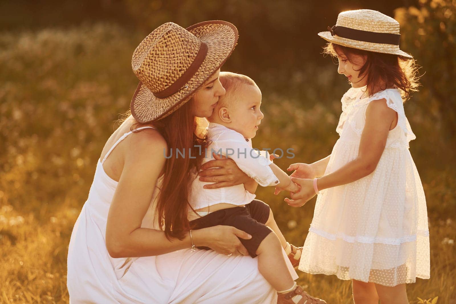 Happy family of mother, little son and daughter spending free time on the field at sunny day time of summer.