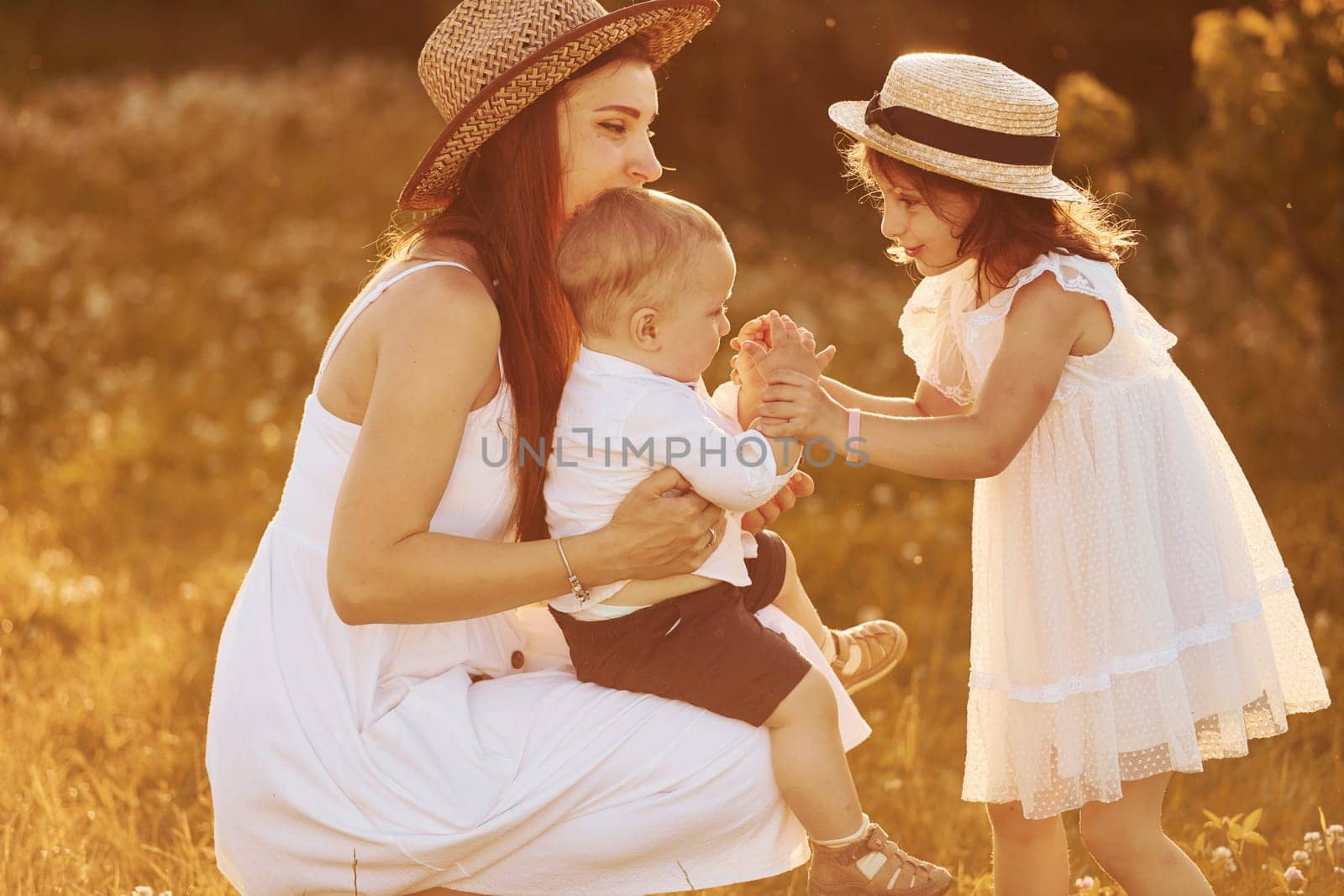 Happy family of mother, little son and daughter spending free time on the field at sunny day time of summer.