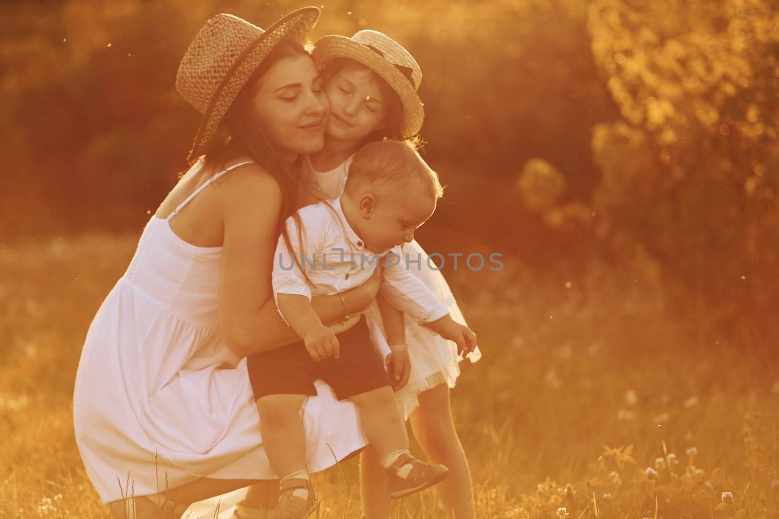 Happy family of mother, little son and daughter spending free time on the field at sunny day time of summer.