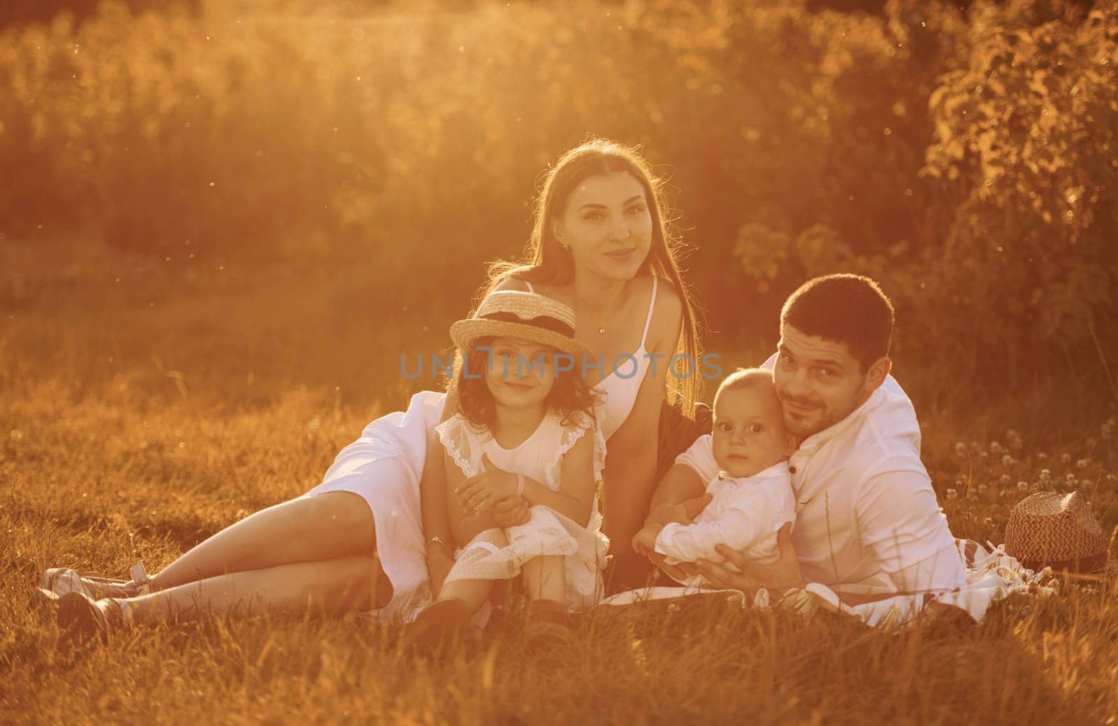 Sitting on the grass. Father, mother with daughter and son spending free time outdoors at sunny day time of summer.