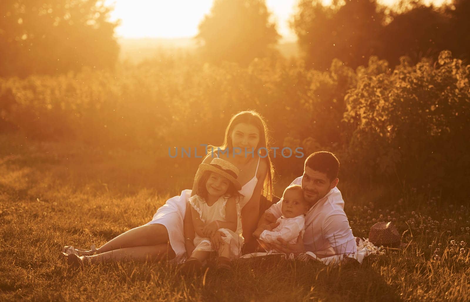 Sitting on the grass. Father, mother with daughter and son spending free time outdoors at sunny day time of summer.