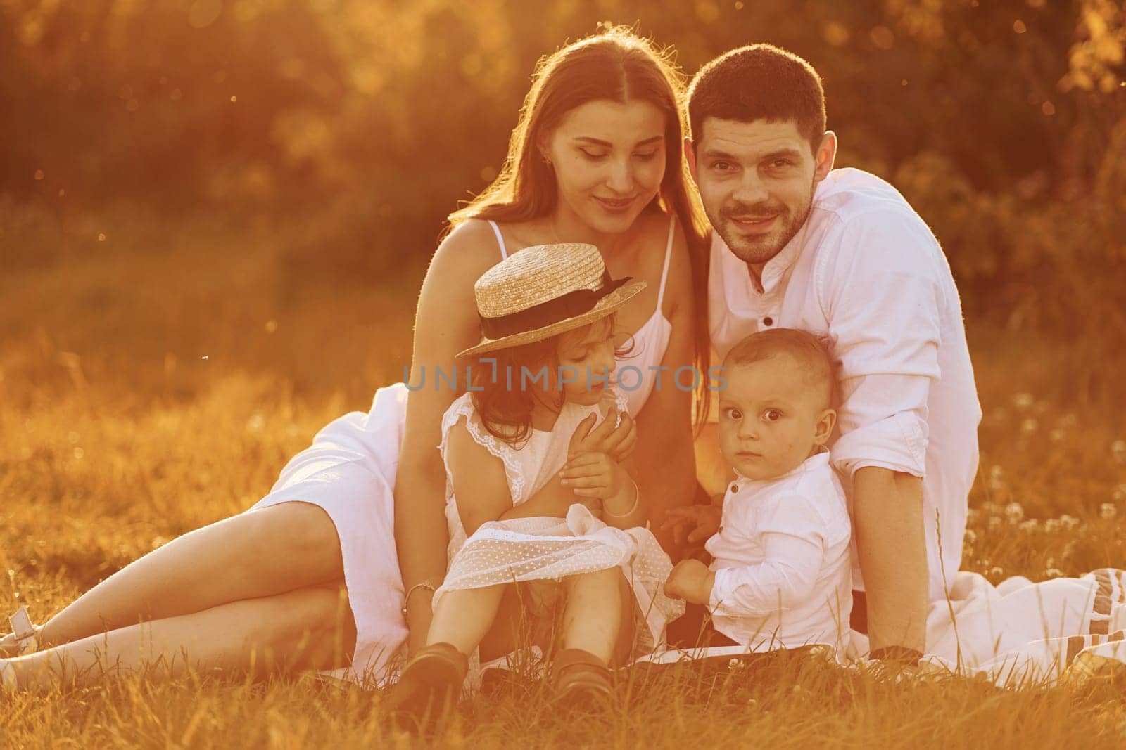 Sitting on the grass. Father, mother with daughter and son spending free time outdoors at sunny day time of summer.