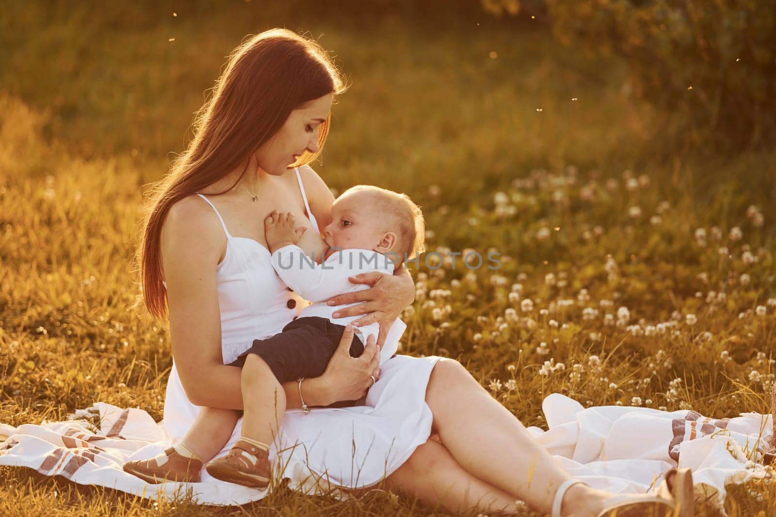 Happy mother breastfeeding her son on the field at sunny day time of summer.