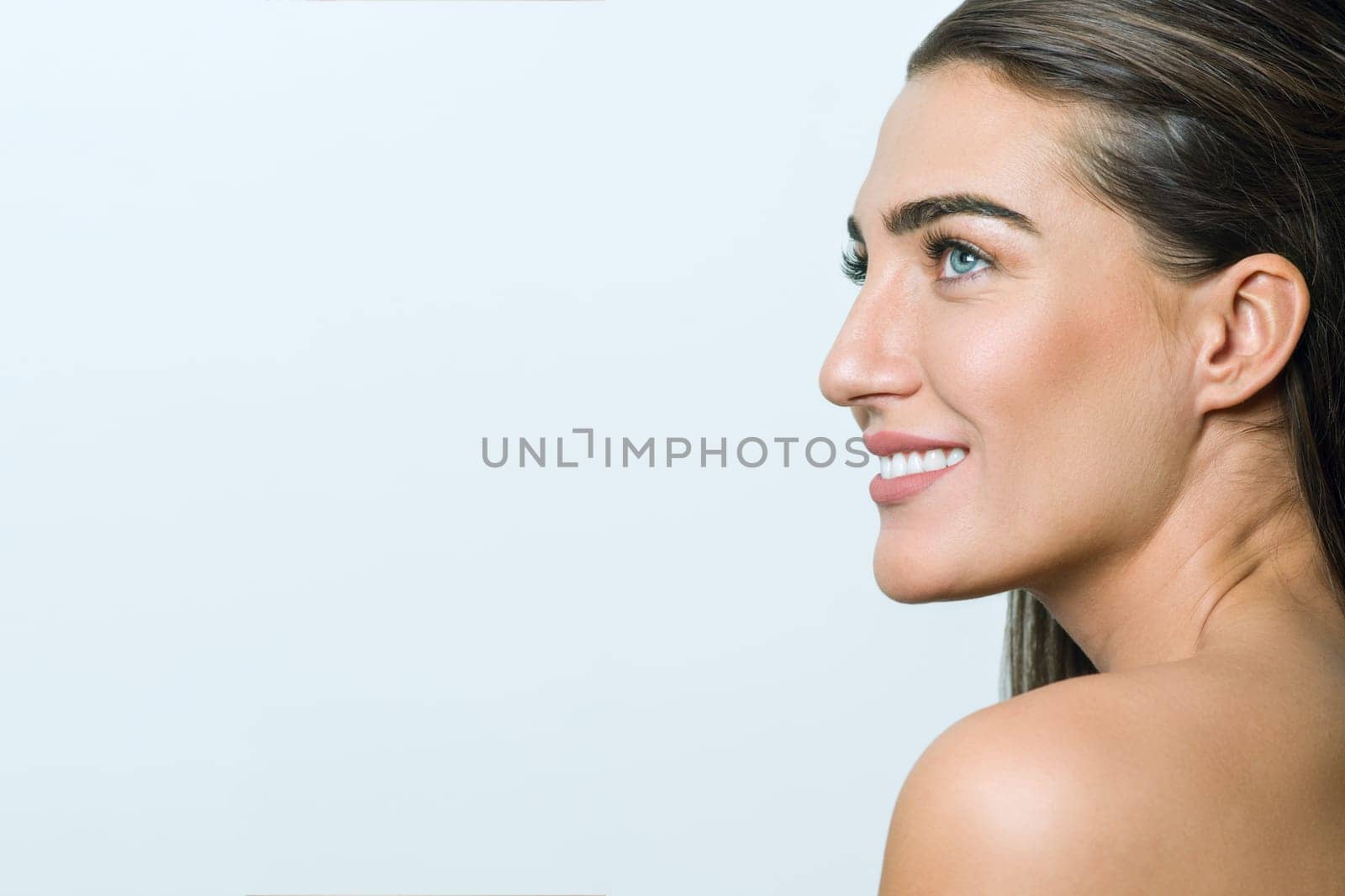 Smiling woman with clean skin, natural make-up, blue eyes, long straight healthy hair and white teeth on white background. Snapshot in profile, copy space