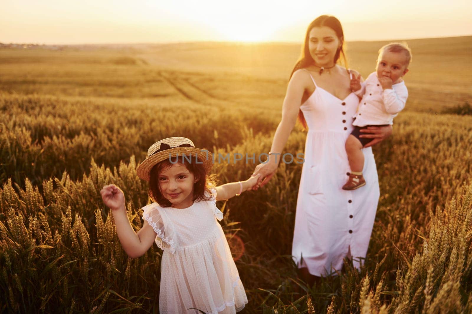 Cheerful family of mother, little son and daughter spending free time on the field at sunny day time of summer.