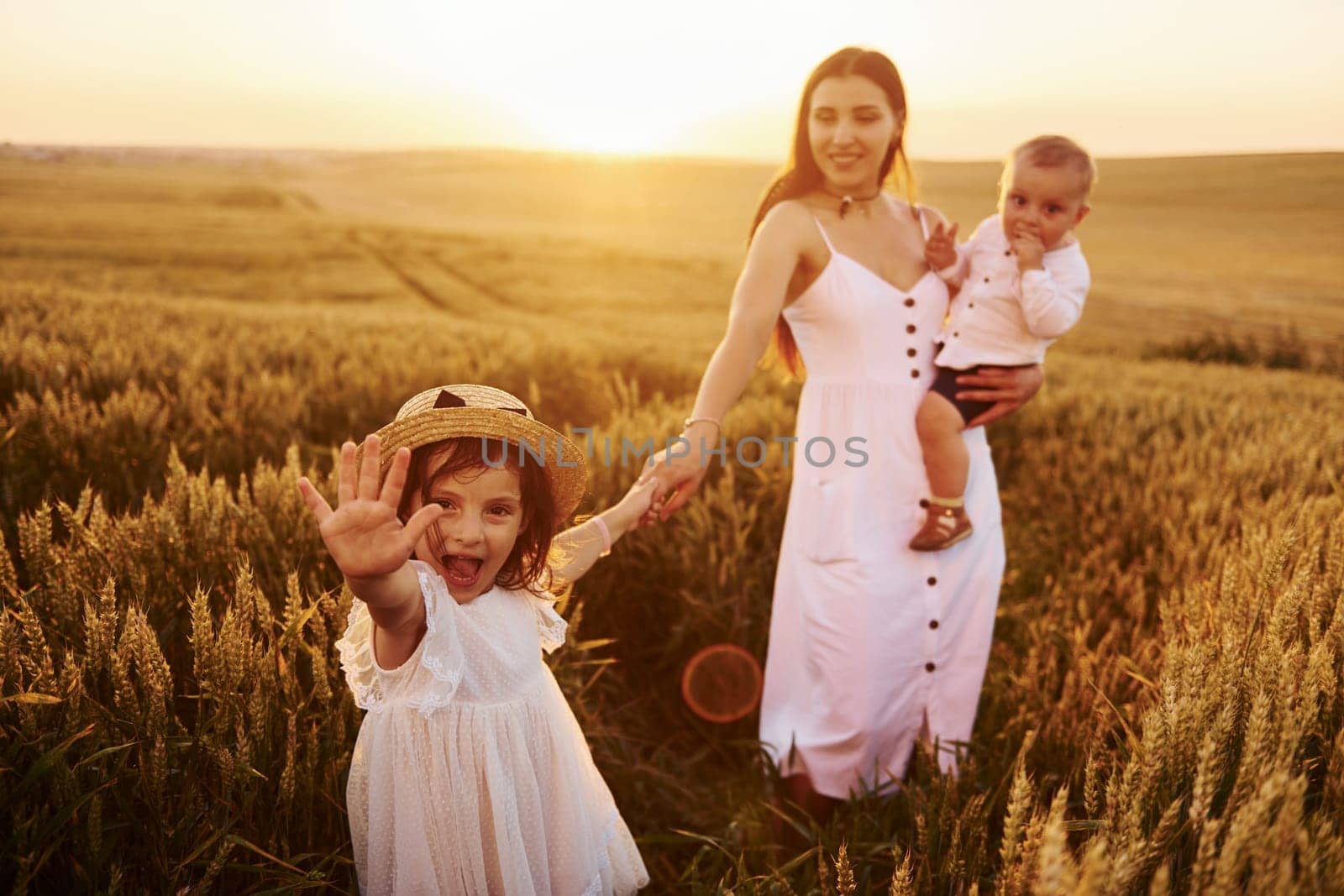 Cheerful family of mother, little son and daughter spending free time on the field at sunny day time of summer.