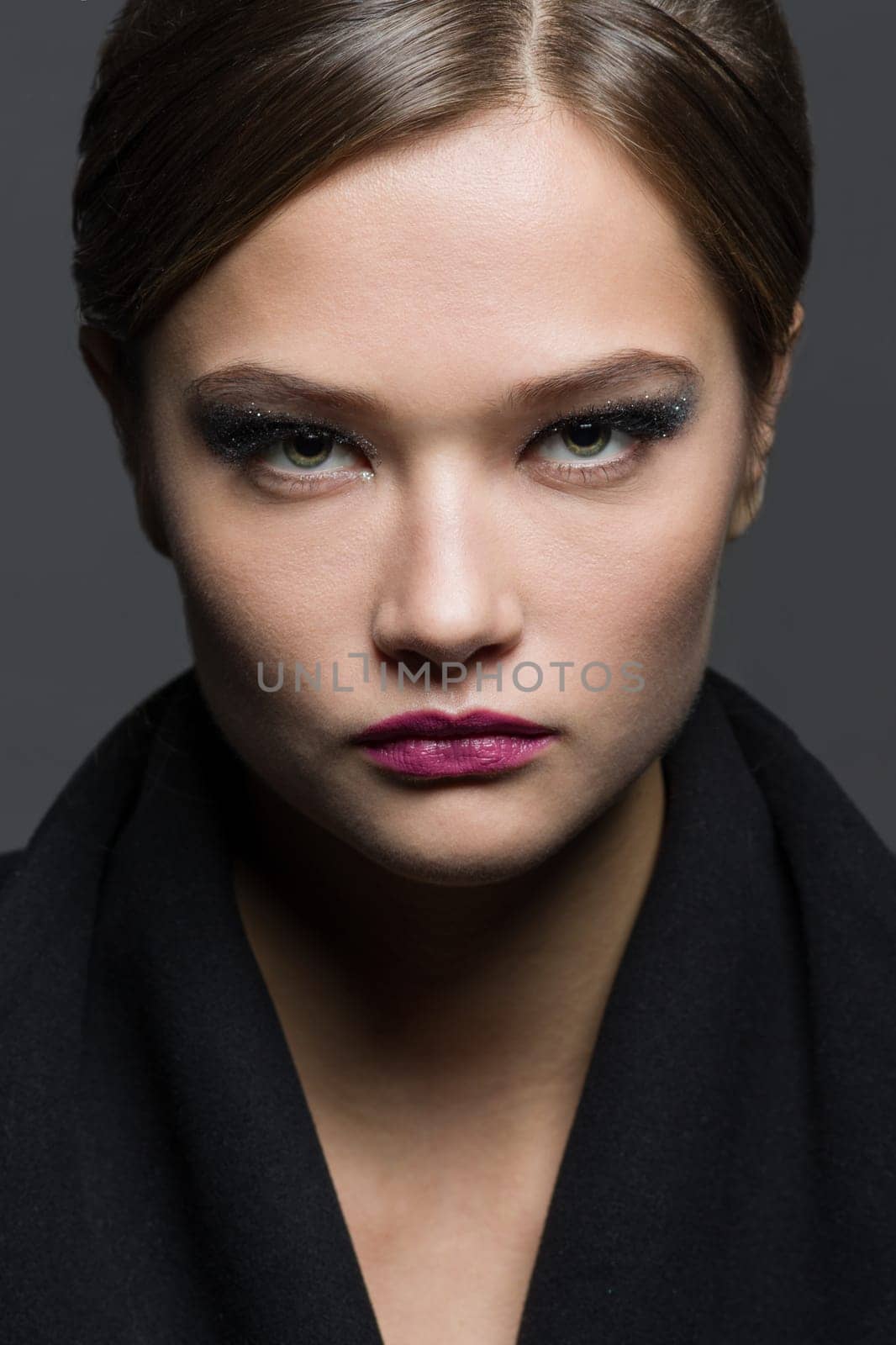 Beauty headshot portrait of a fashionable young woman with glamorous makeup and hairstyle, on a gray studio background