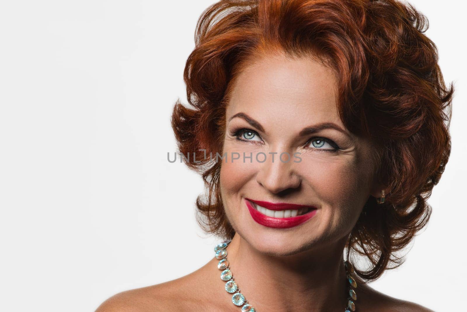 Portrait of beautiful redhead middle aged woman with hairstyle and makeup looking to the side, on white isolated. Head shot of a smiling woman with teeth