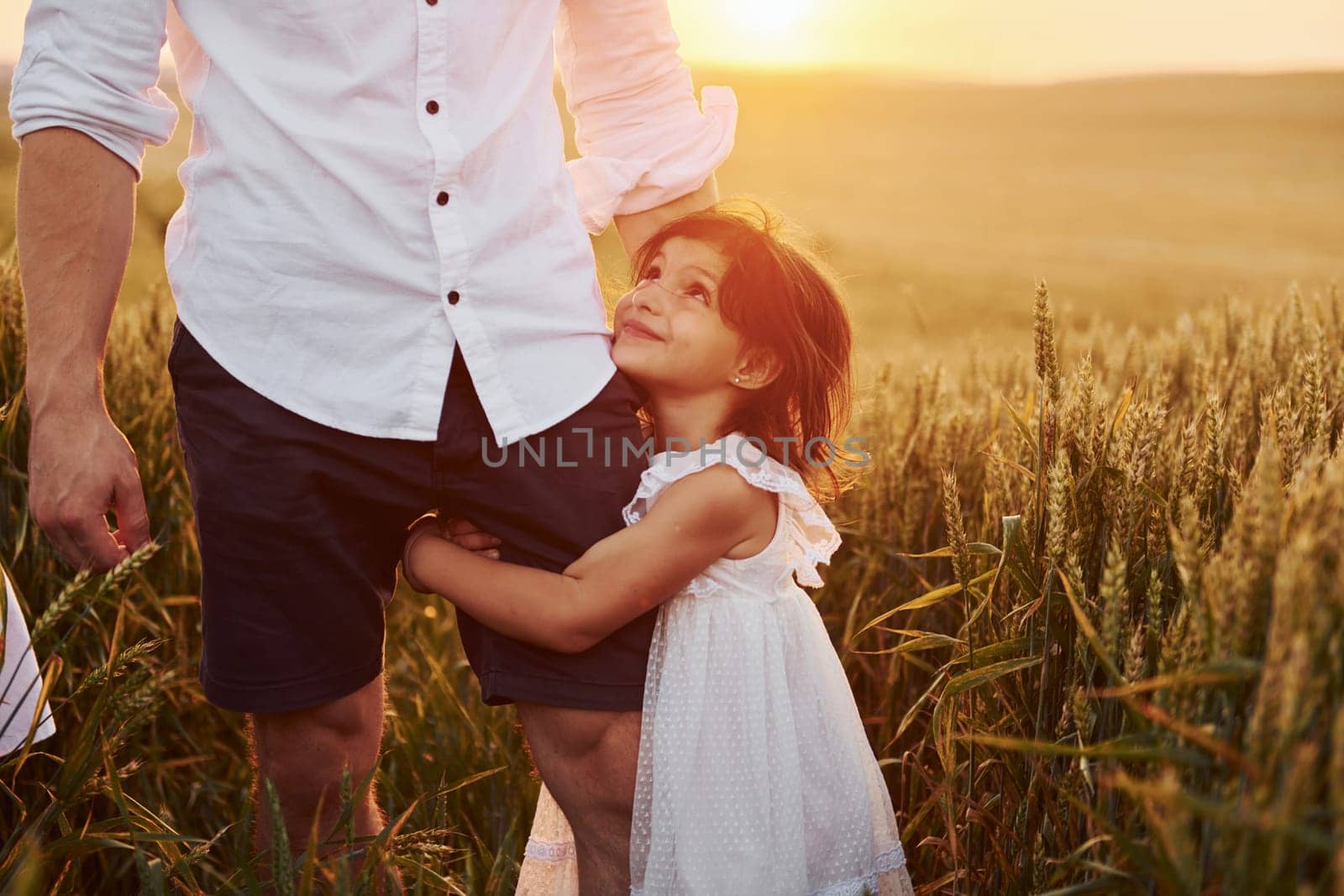 Girl embraces parent. Father with daughter spending free time on the field at sunny day time of summer.