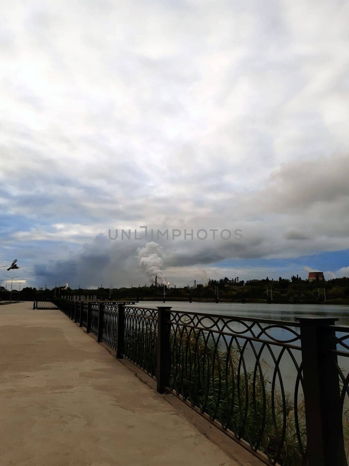 City embankment against the backdrop of a reservoir and a metallurgical plant in the early morning.