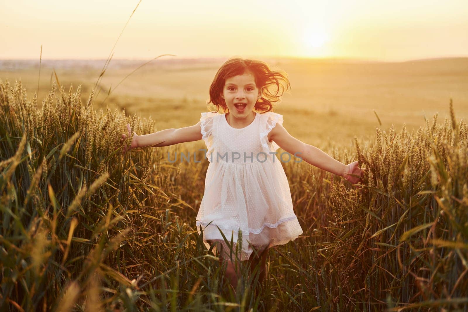 Cheerful little girl in white dress running in the agricultural field at summer day time by Standret