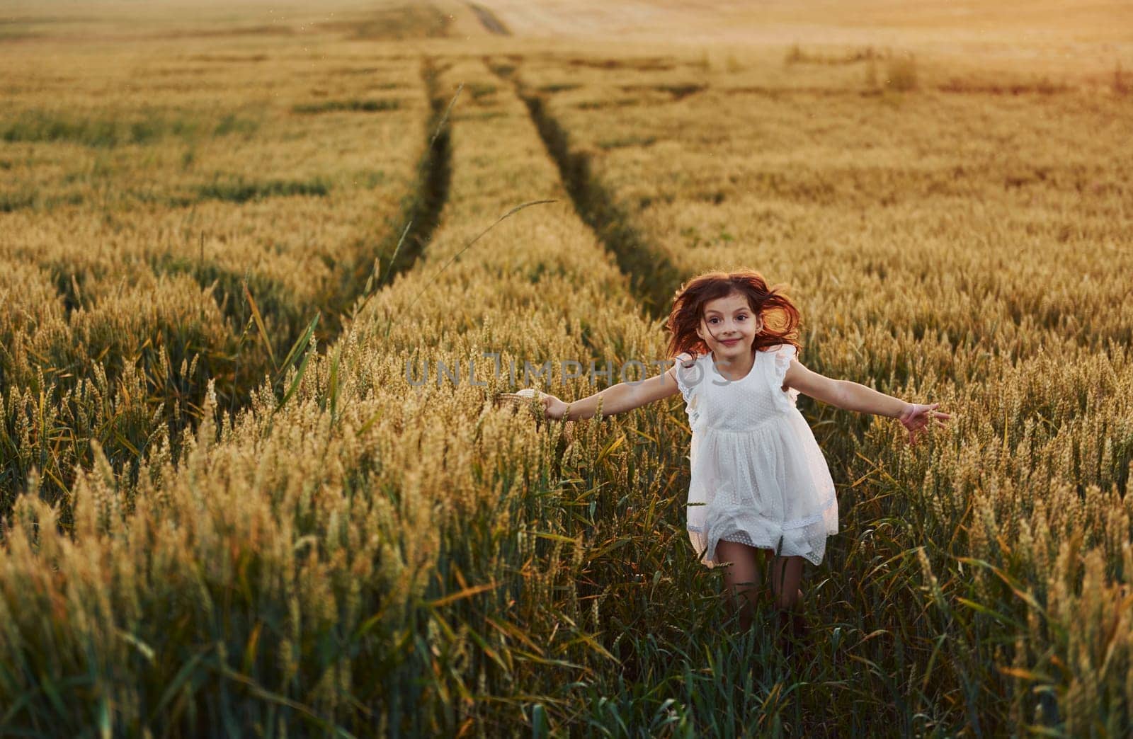 Cheerful little girl in white dress running in the agricultural field at summer day time by Standret