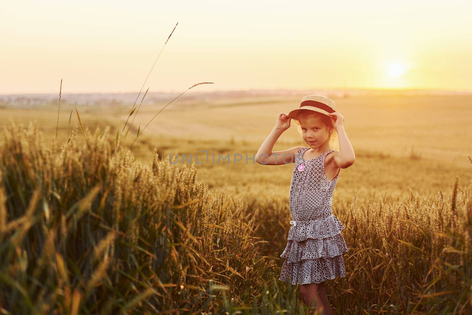 Little girl standing on the agricultural field at evening time. Conception of summer free time.