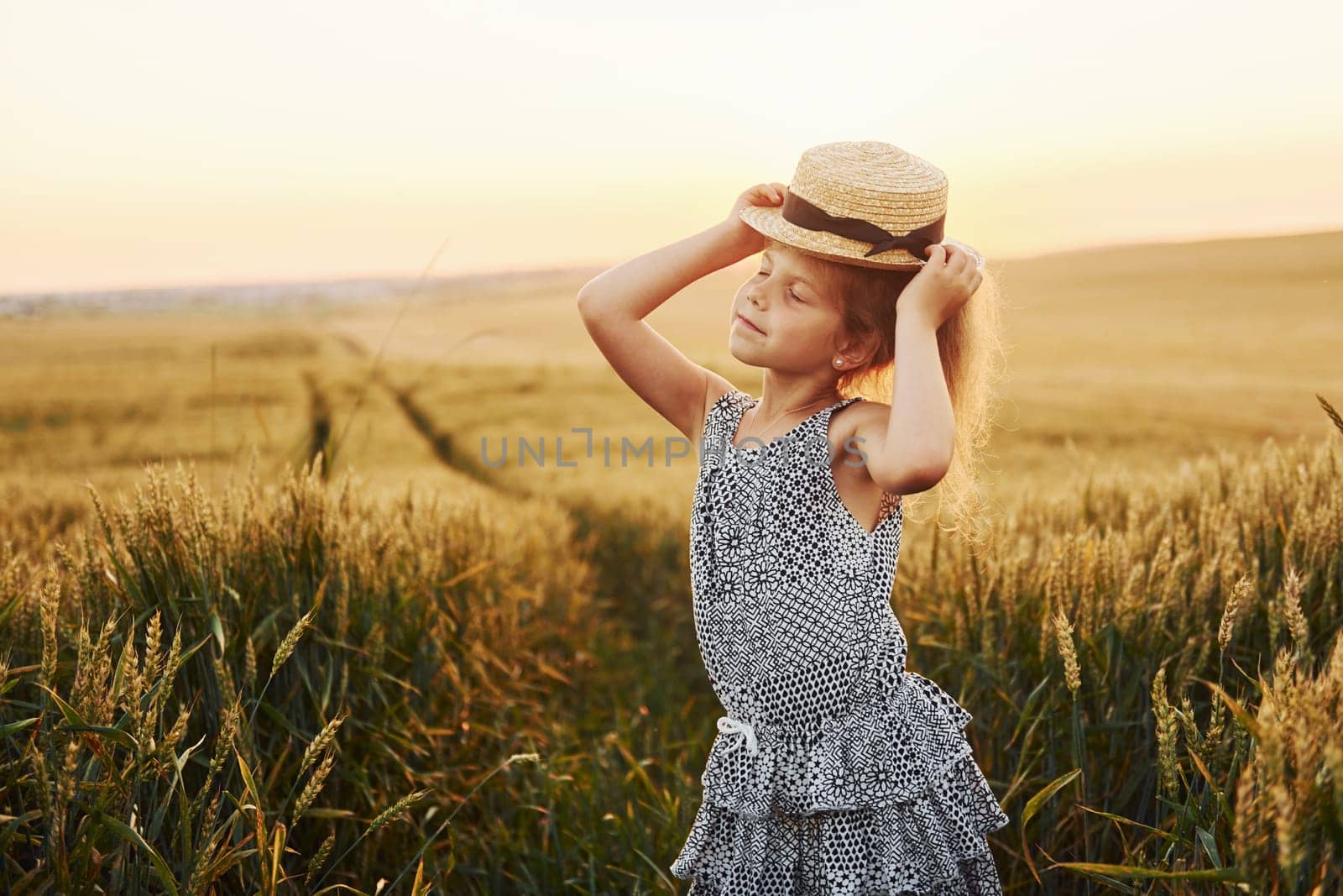 Little girl standing on the agricultural field at evening time. Conception of summer free time.