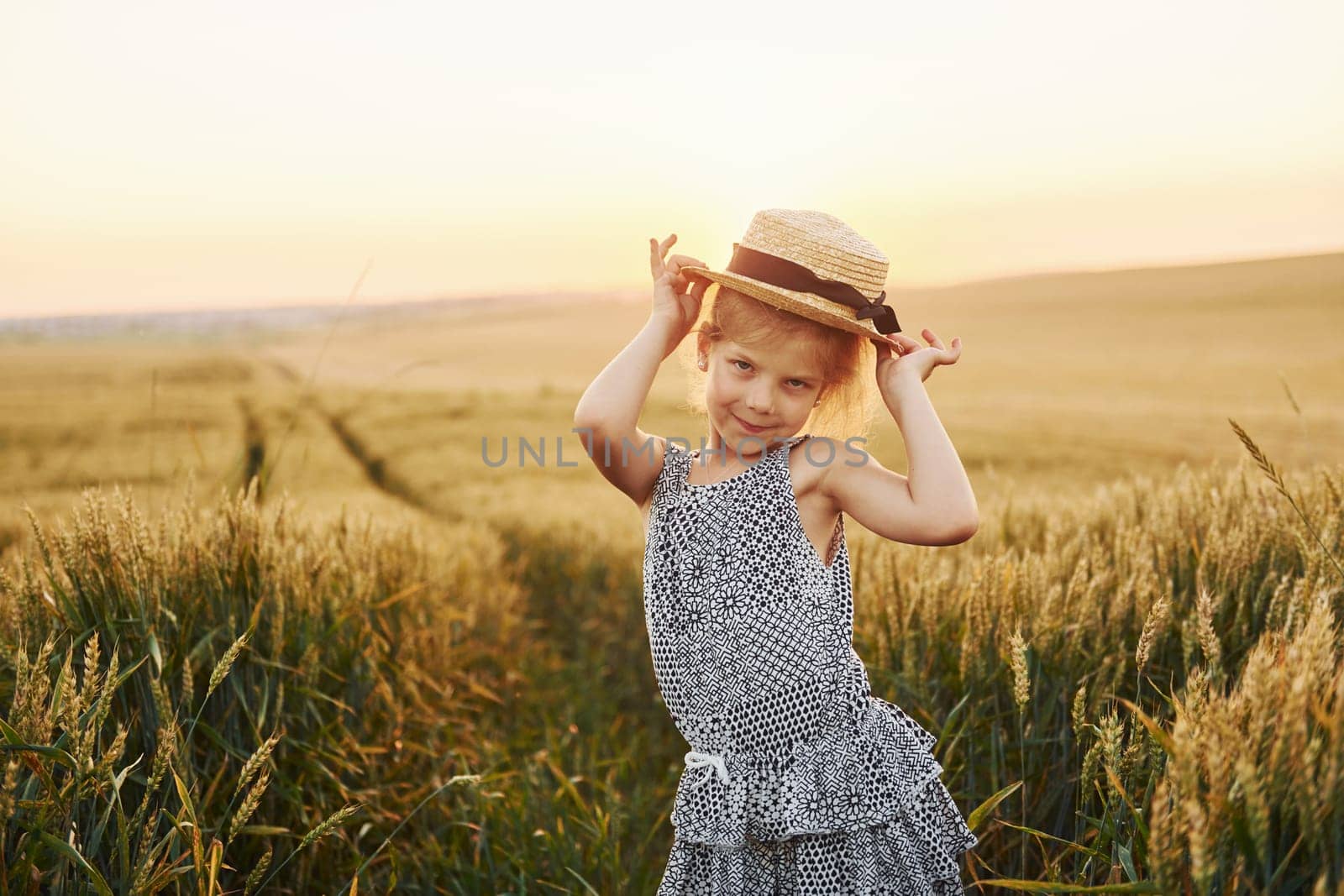 Little girl standing on the agricultural field at evening time. Conception of summer free time.