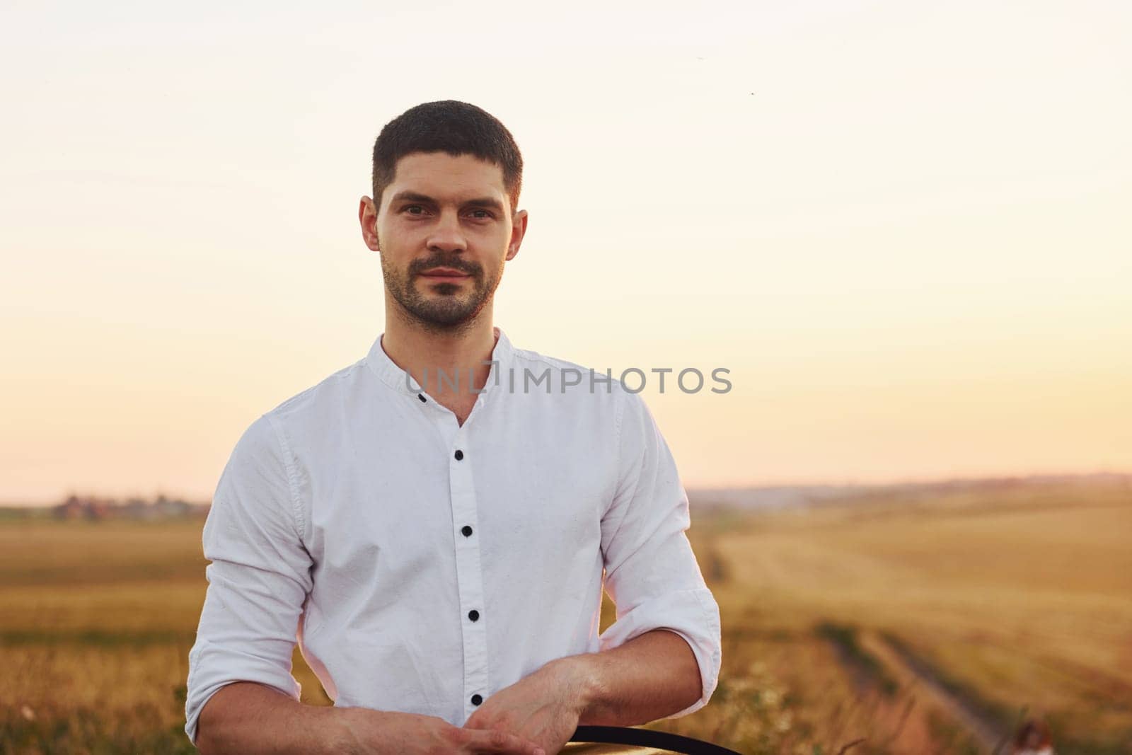 Portrait of man in white shirt that standing on the field at evening time.