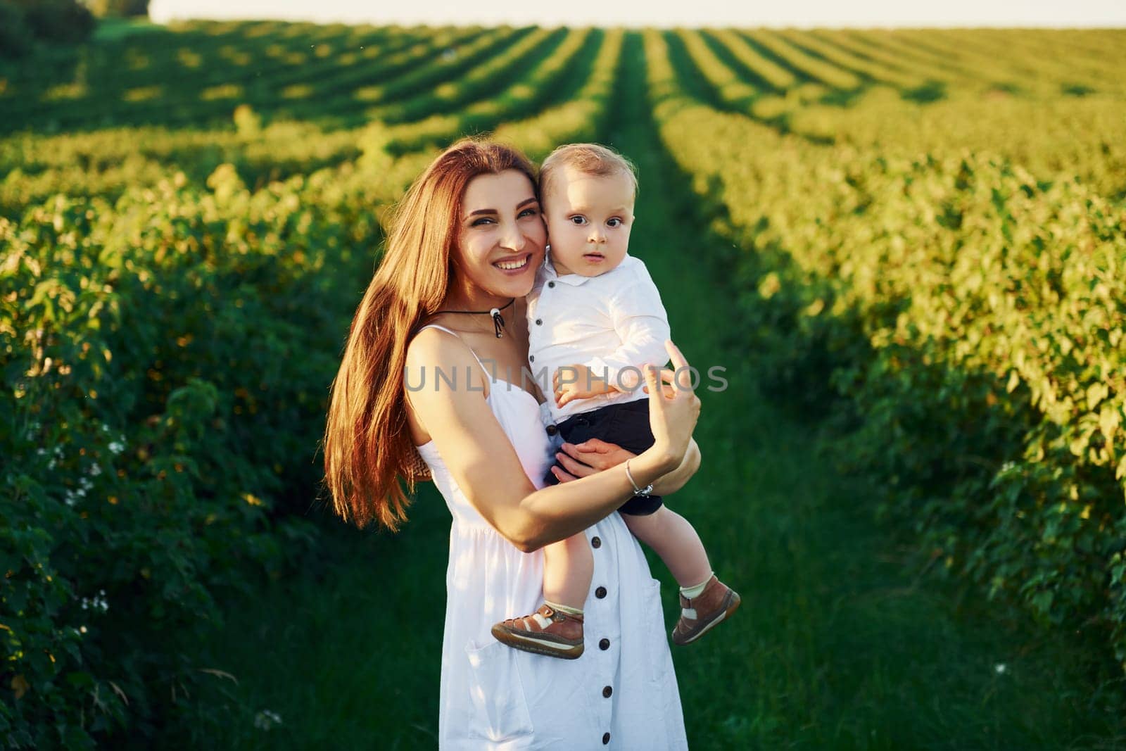 Positive mother with her son spending free time on the field at sunny day time of summer.
