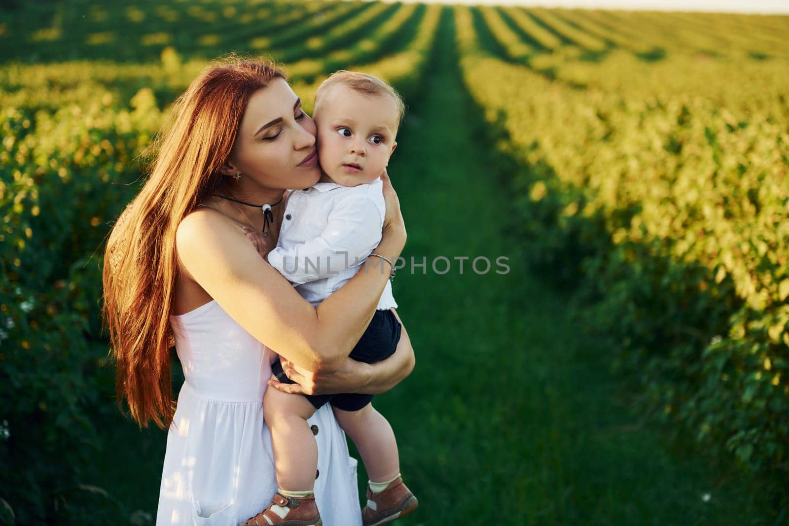 Positive mother with her son spending free time on the field at sunny day time of summer.
