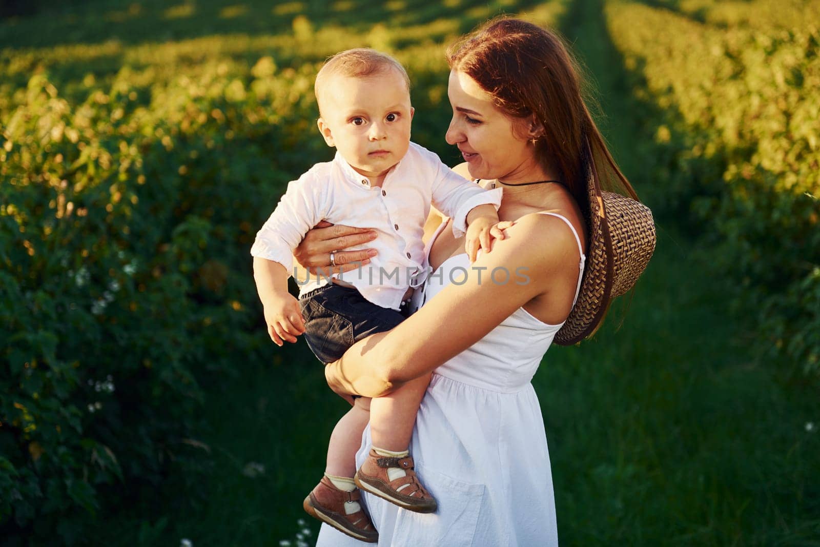 Positive mother with her son spending free time on the field at sunny day time of summer.