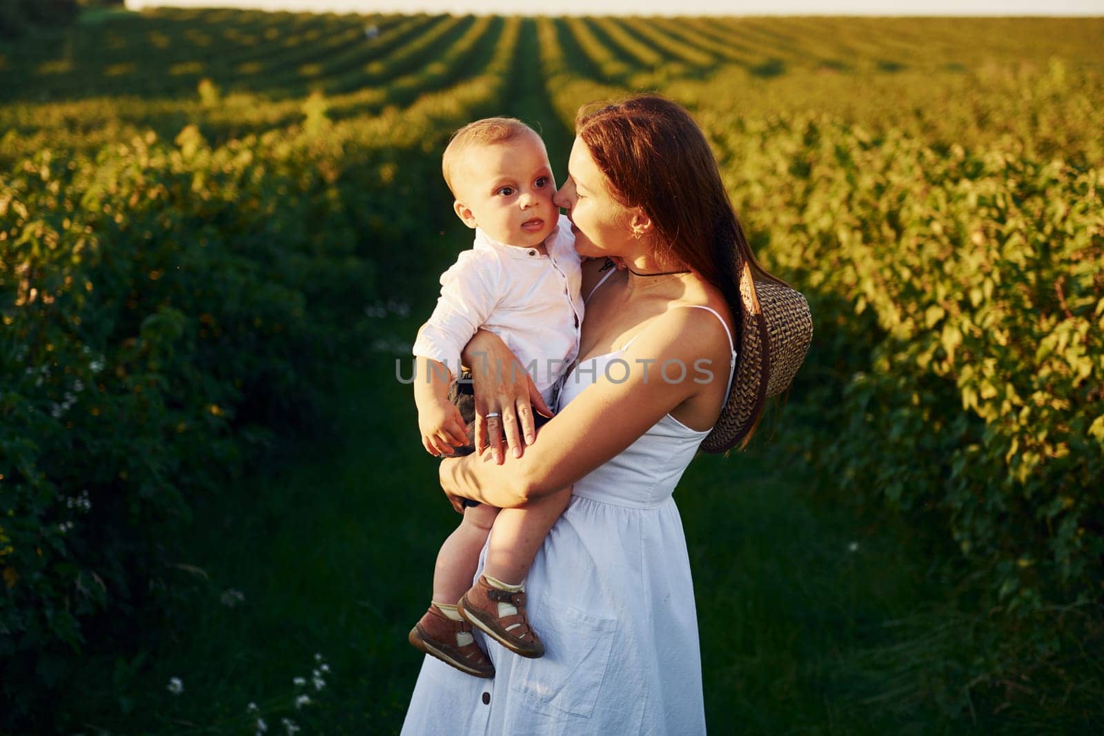 Positive mother with her son spending free time on the field at sunny day time of summer.